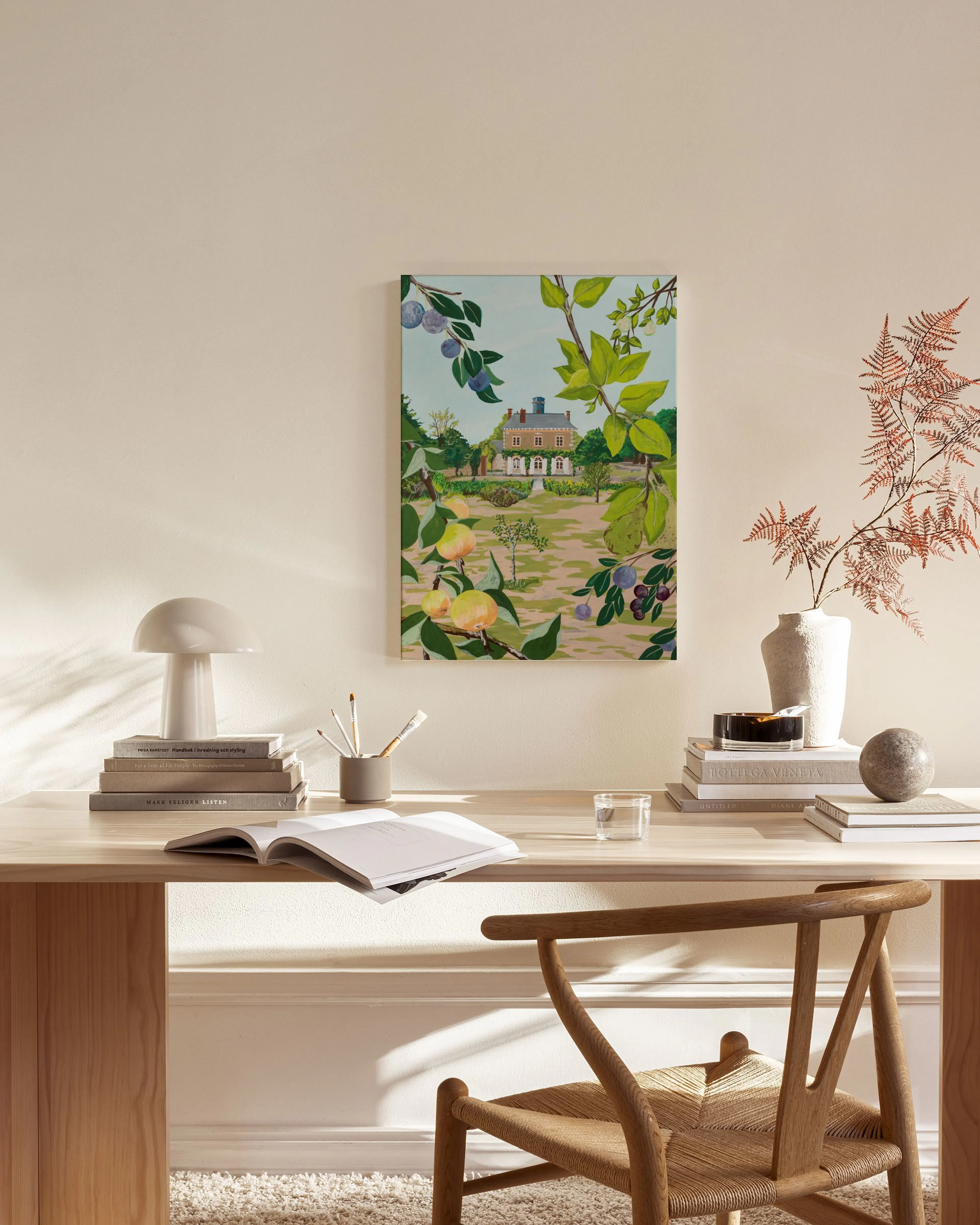 Lienzo con una casa de campo rodeada de árboles frutales, colgando sobre un mueble bajo junto a un sillón y una mesa de centro e
