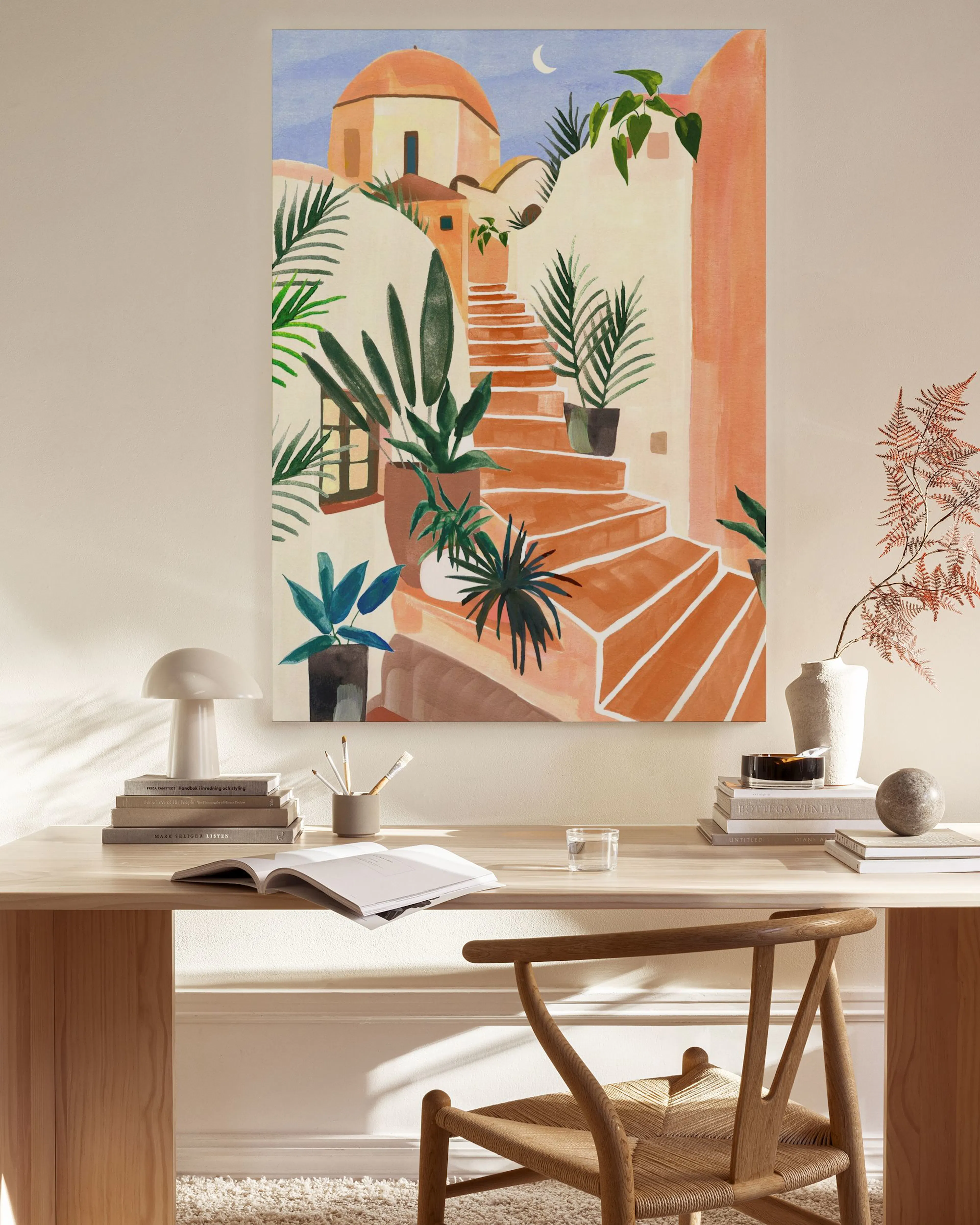 Lienzo con ilustración de escaleras de terracota en un pueblo mediterráneo con plantas, colgado en una pared clara sobre un mueb