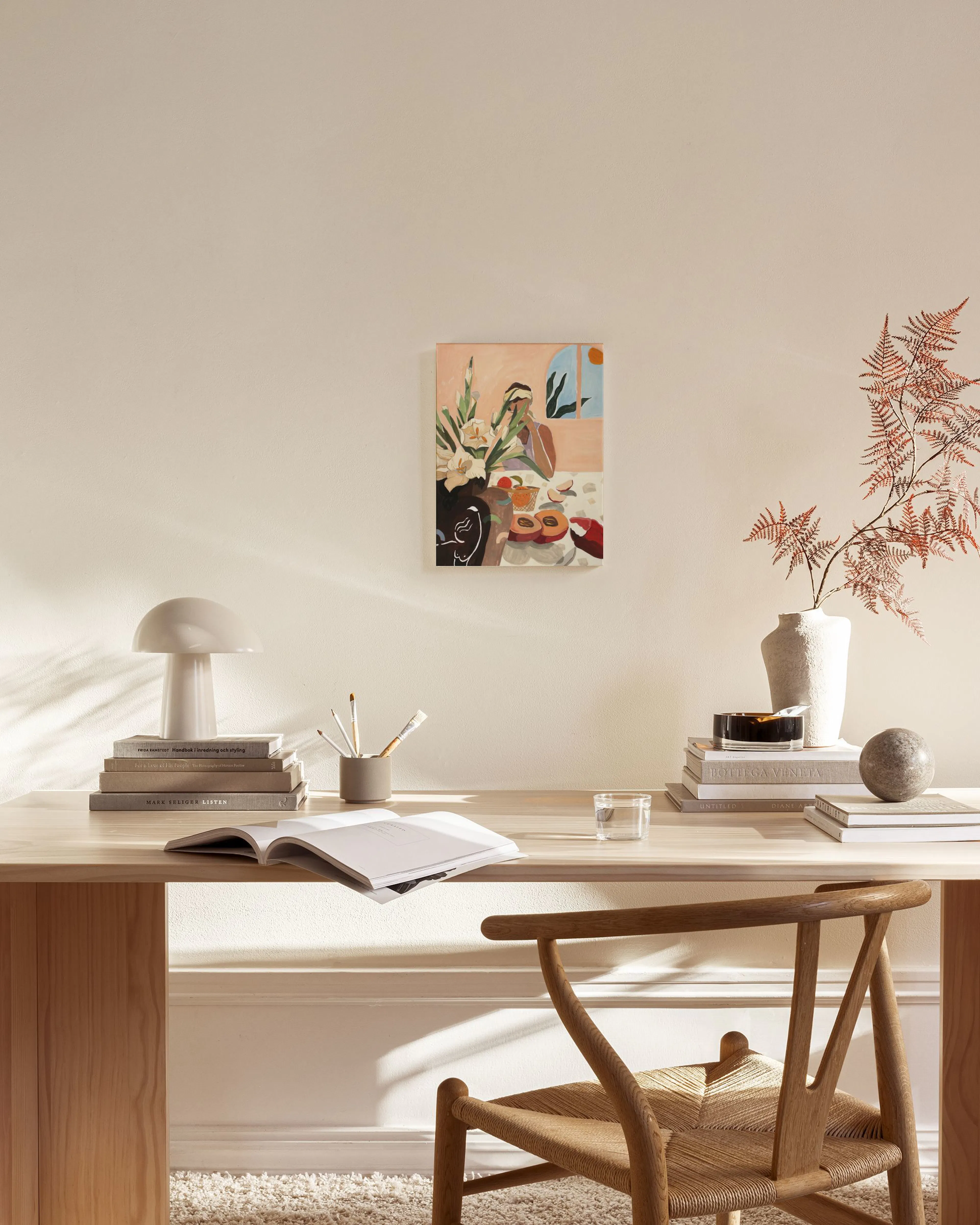 Lærred med illustration af en kvinde ved et bord med frugt og blomster, hængende i en stue.