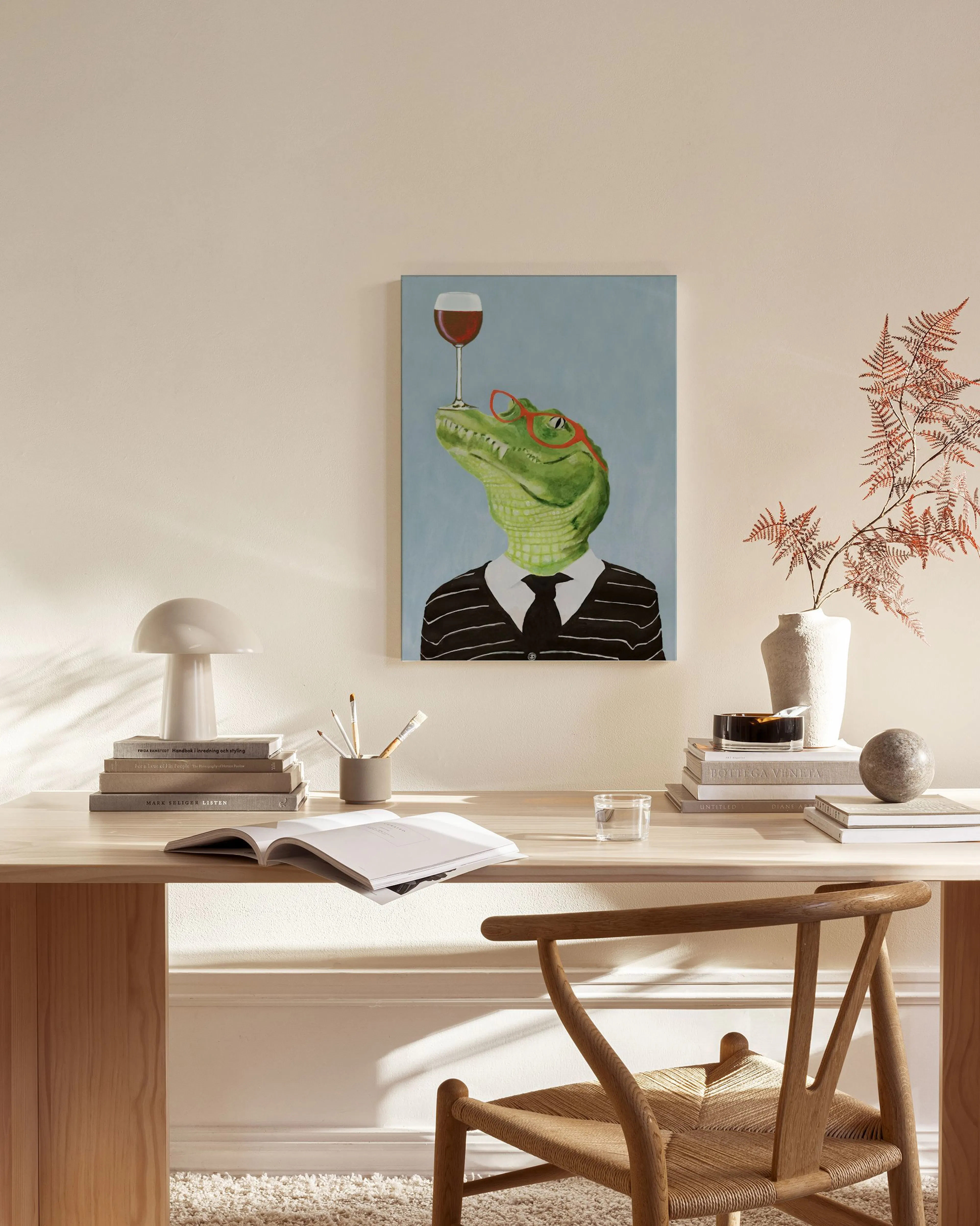 Canvastavla med en elegant kostymklädd krokodil i röda glasögon som balanserar ett vinglas. Hänger i ett ljust vardagsrum.
