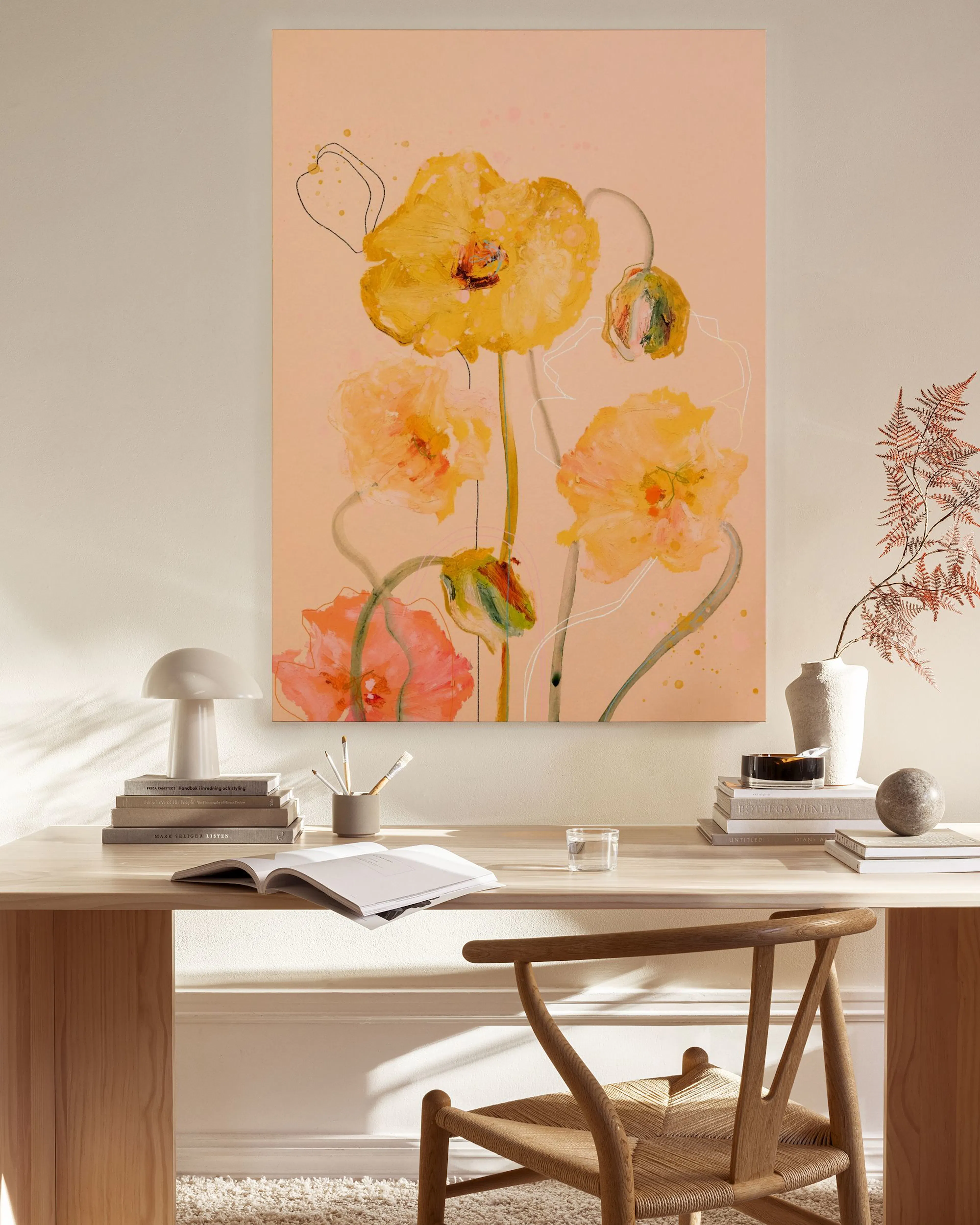 A canvas print of watercolor poppies in shades of yellow and orange on a pink background, displayed above a light wood console t