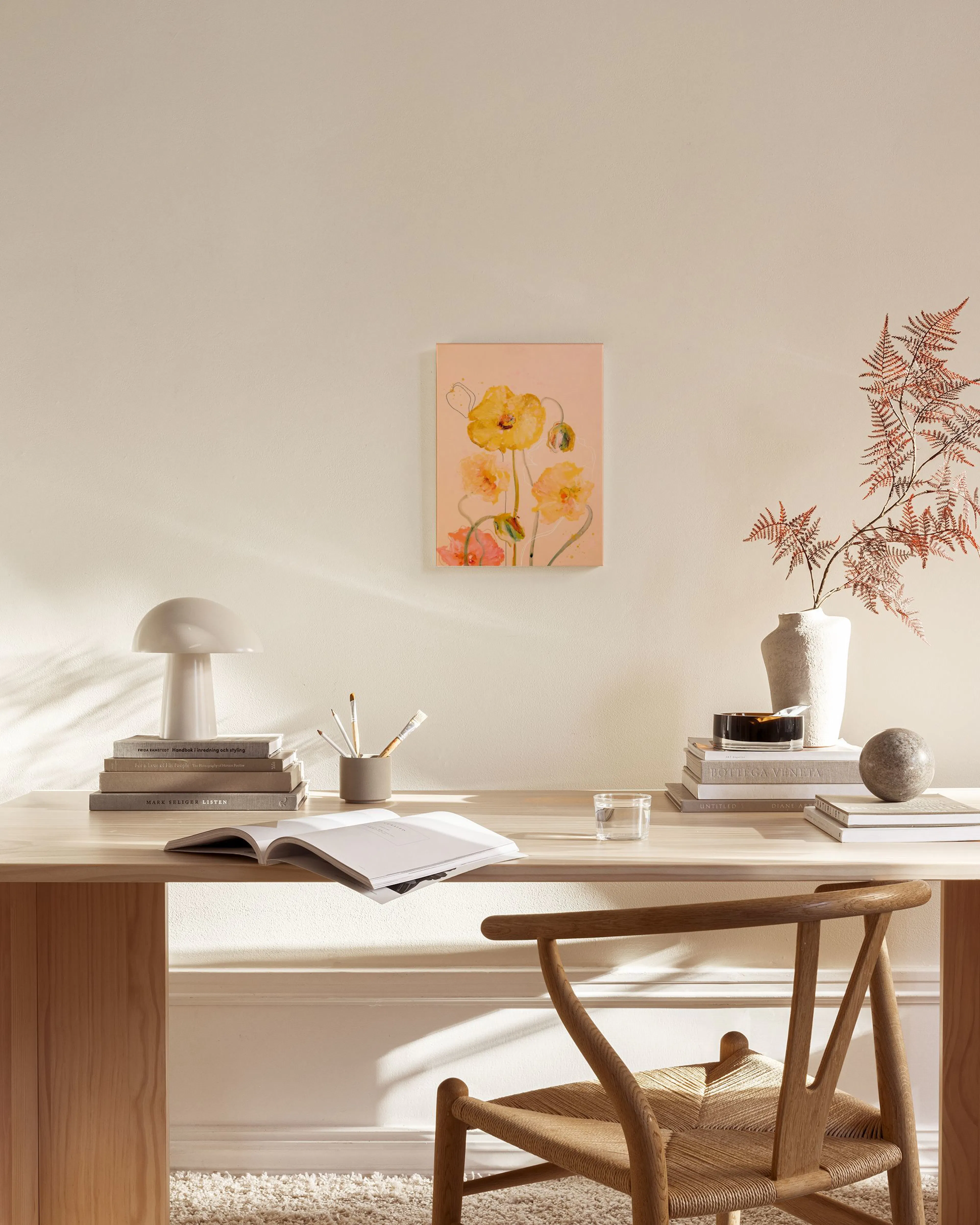 A canvas print of watercolor poppies in shades of yellow and orange on a pink background, displayed above a light wood console t
