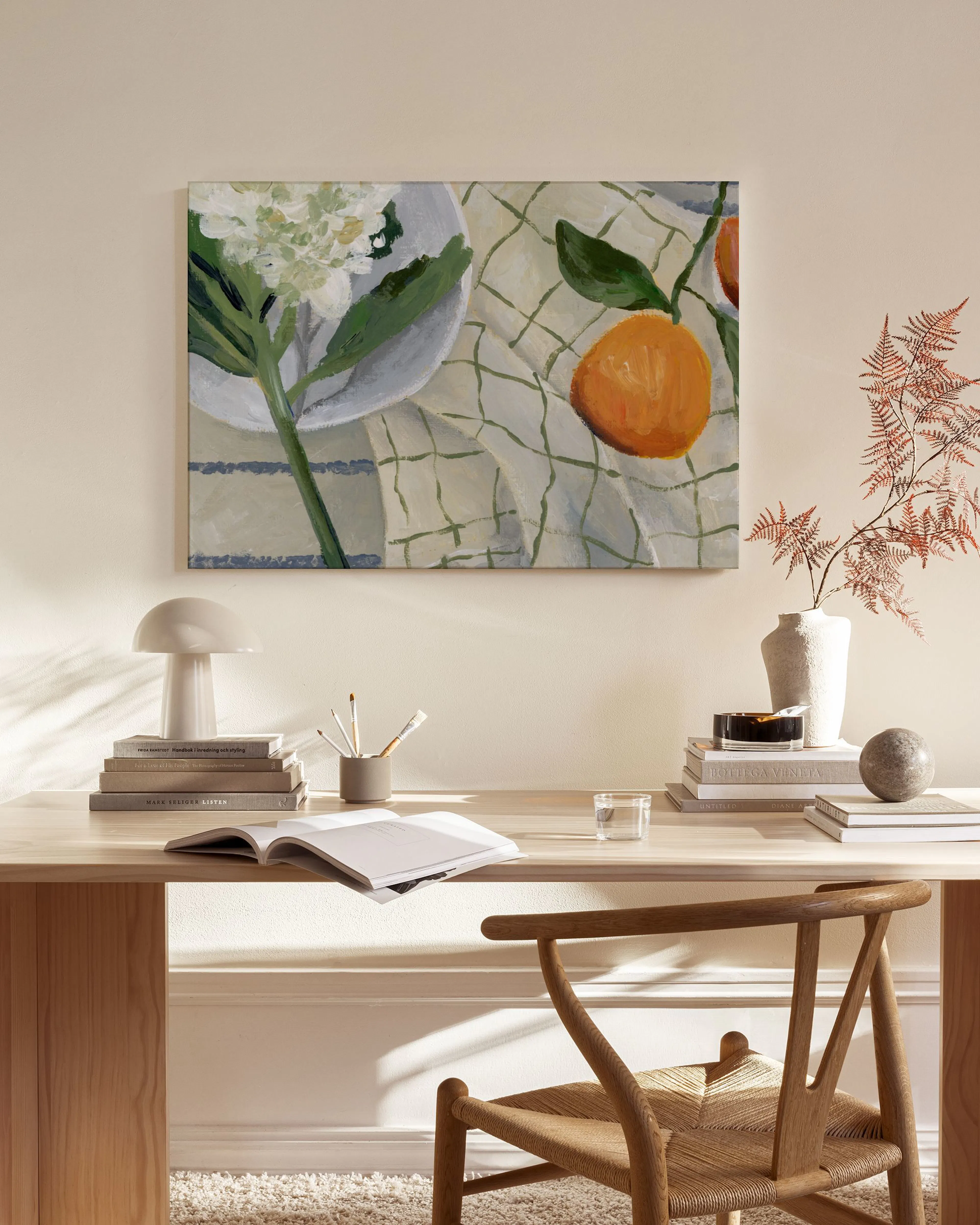 A still life canvas print of white flowers and oranges on a checkered tablecloth, displayed above a wooden console table in a mi
