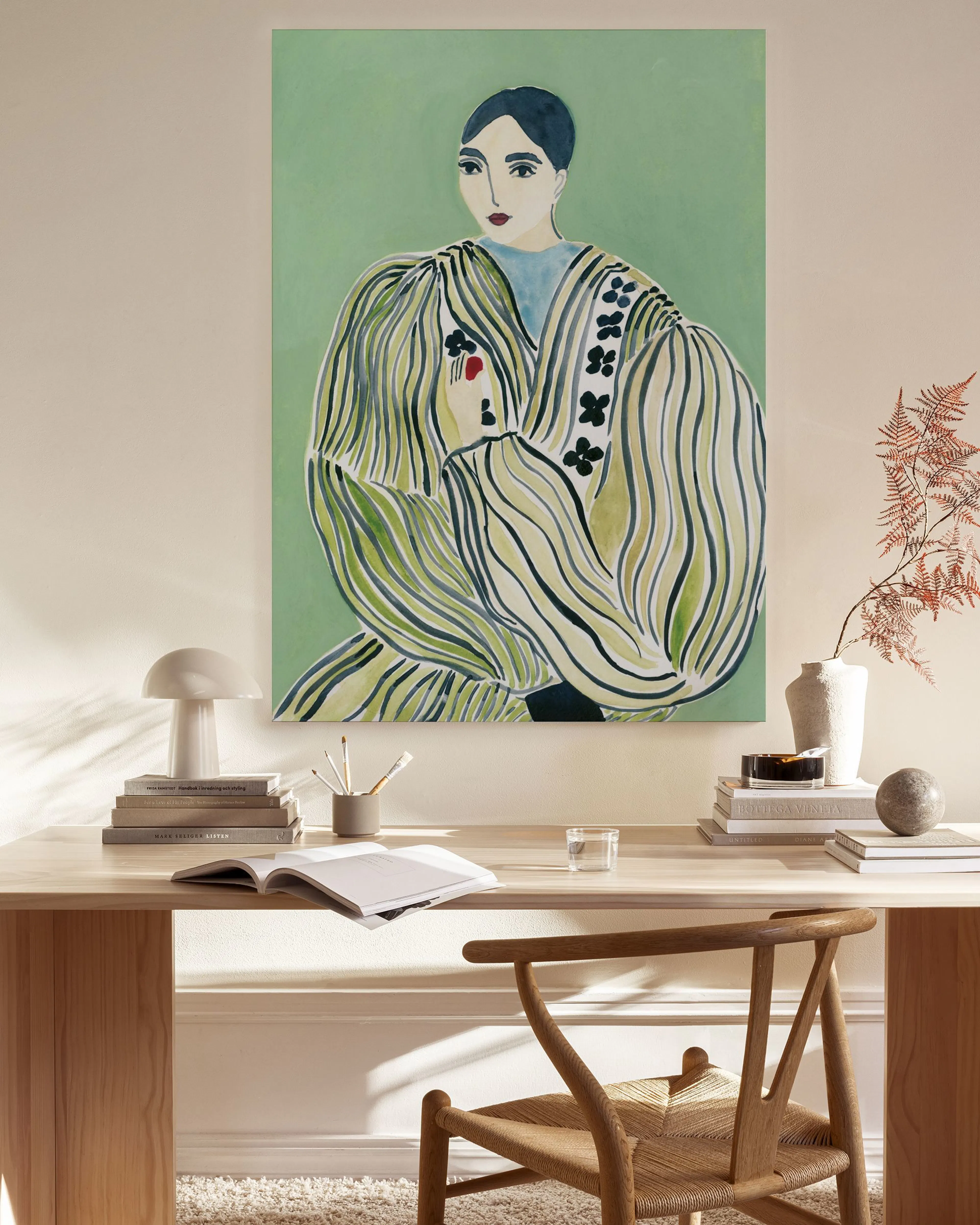Toile dune femme en robe verte et blanche sur un mur clair, au-dessus dun banc en bois avec une lampe et des livres.