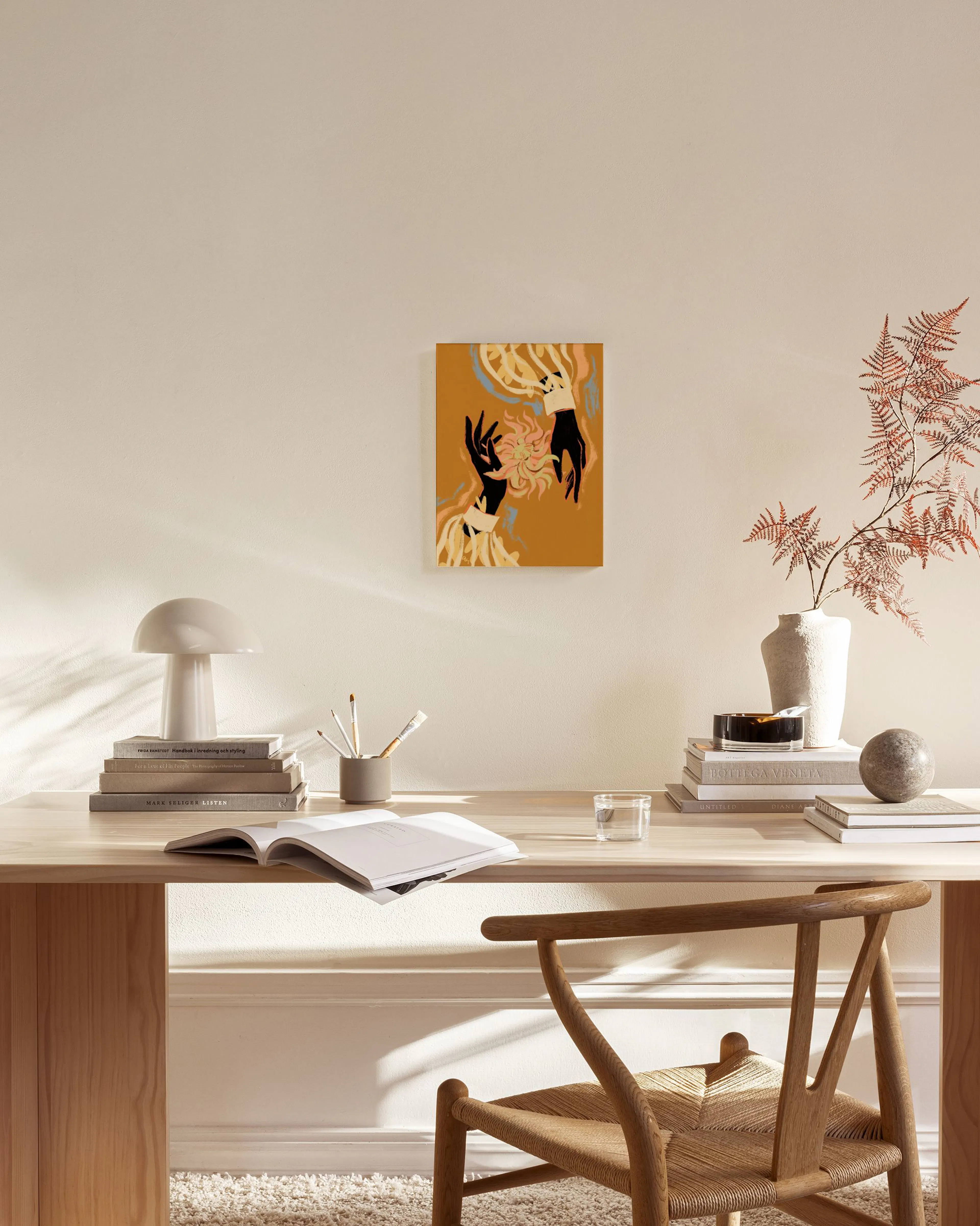 Leinwandbild mit orangem Hintergrund und zwei schwarzen Händen, die eine goldene Blüte halten, hängt im Wohnzimmer.