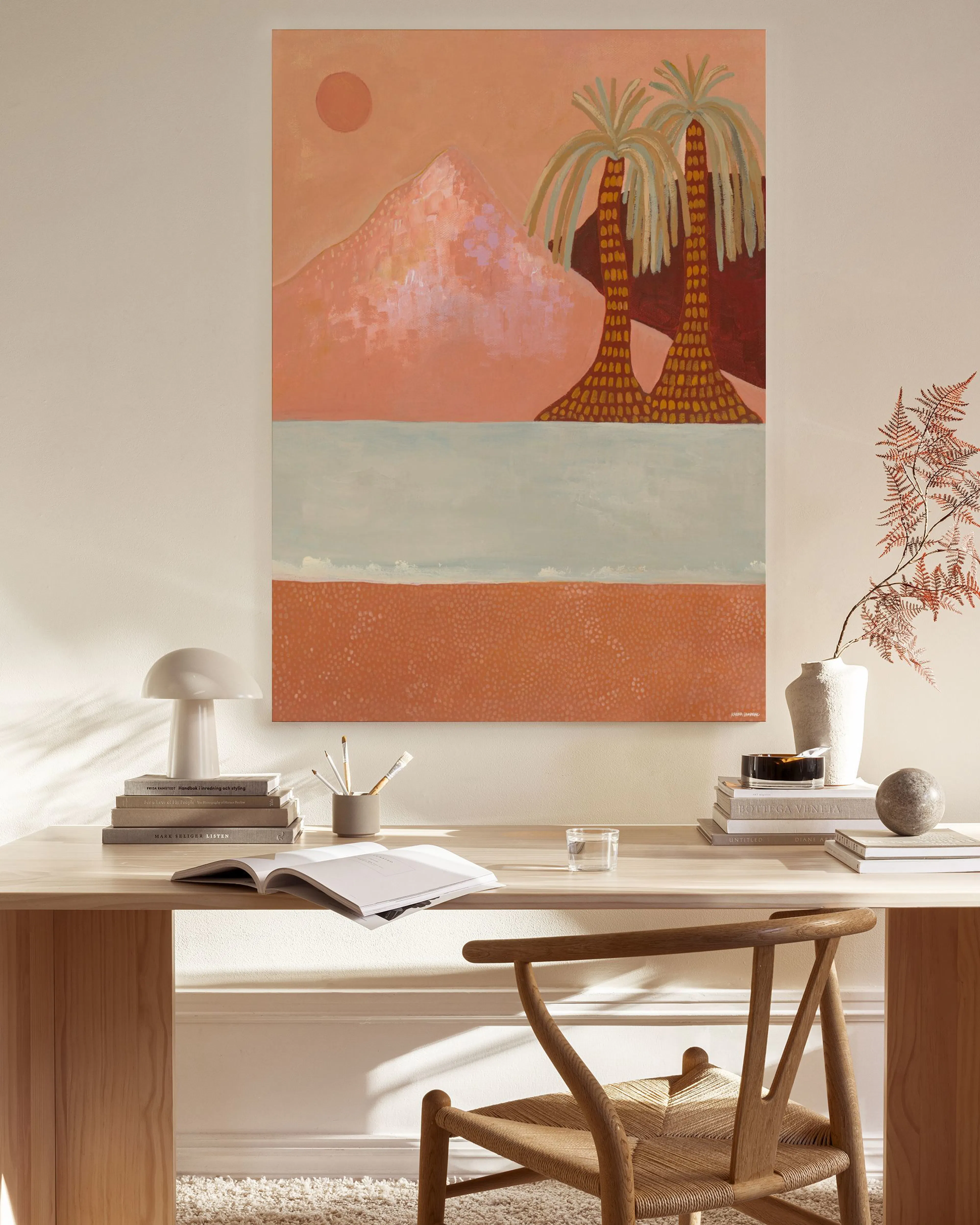 Canvas met roze berg, palmbomen en water, hangend boven een houten dressoir in een lichte woonkamer.