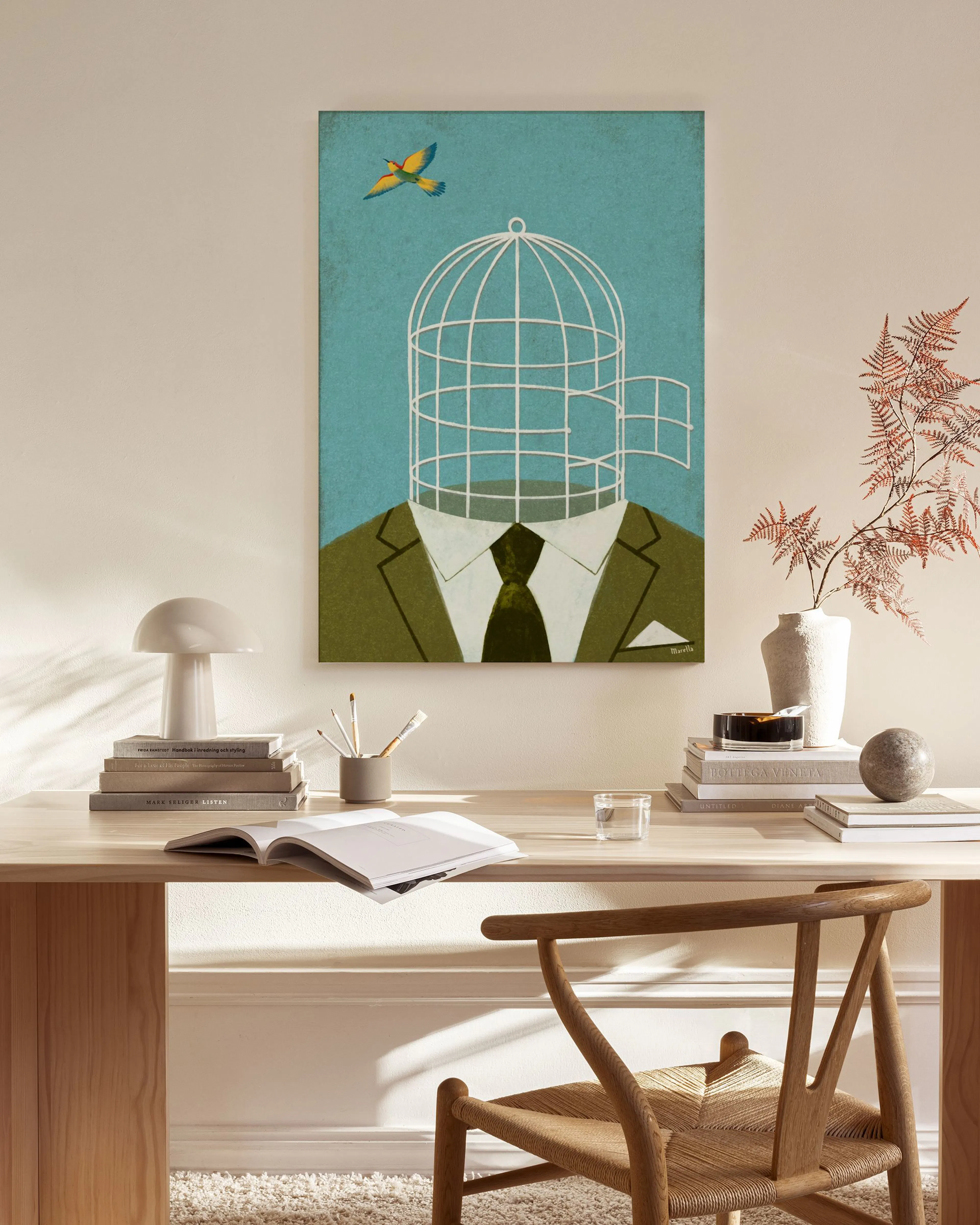 A print of a man in a green suit with a birdcage for a head and a bird flying free, hanging in a minimalist living room.
