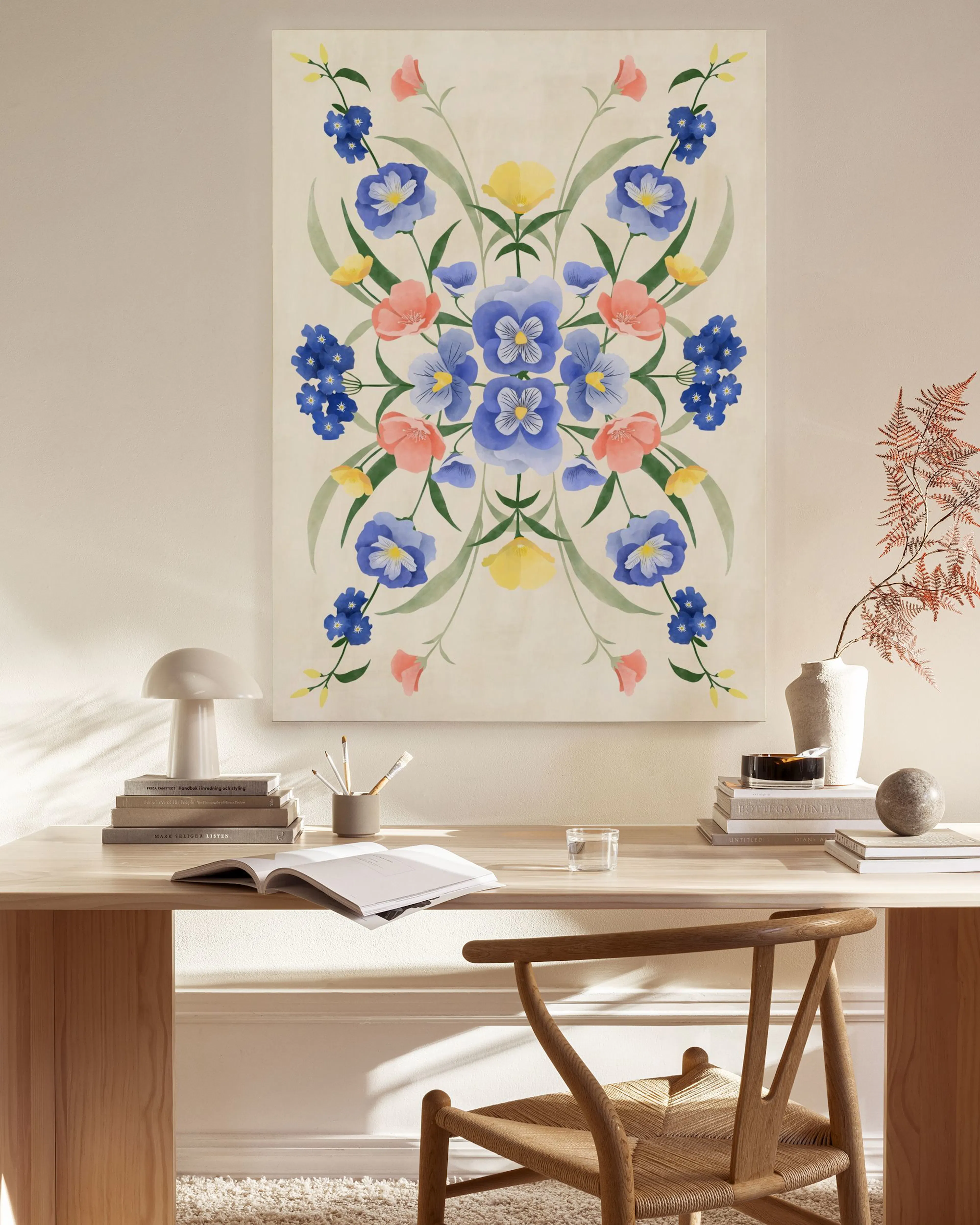 Canvas met symmetrisch patroon van blauwe en roze bloemen, en gele bladeren, hangend in een lichte woonkamer.
