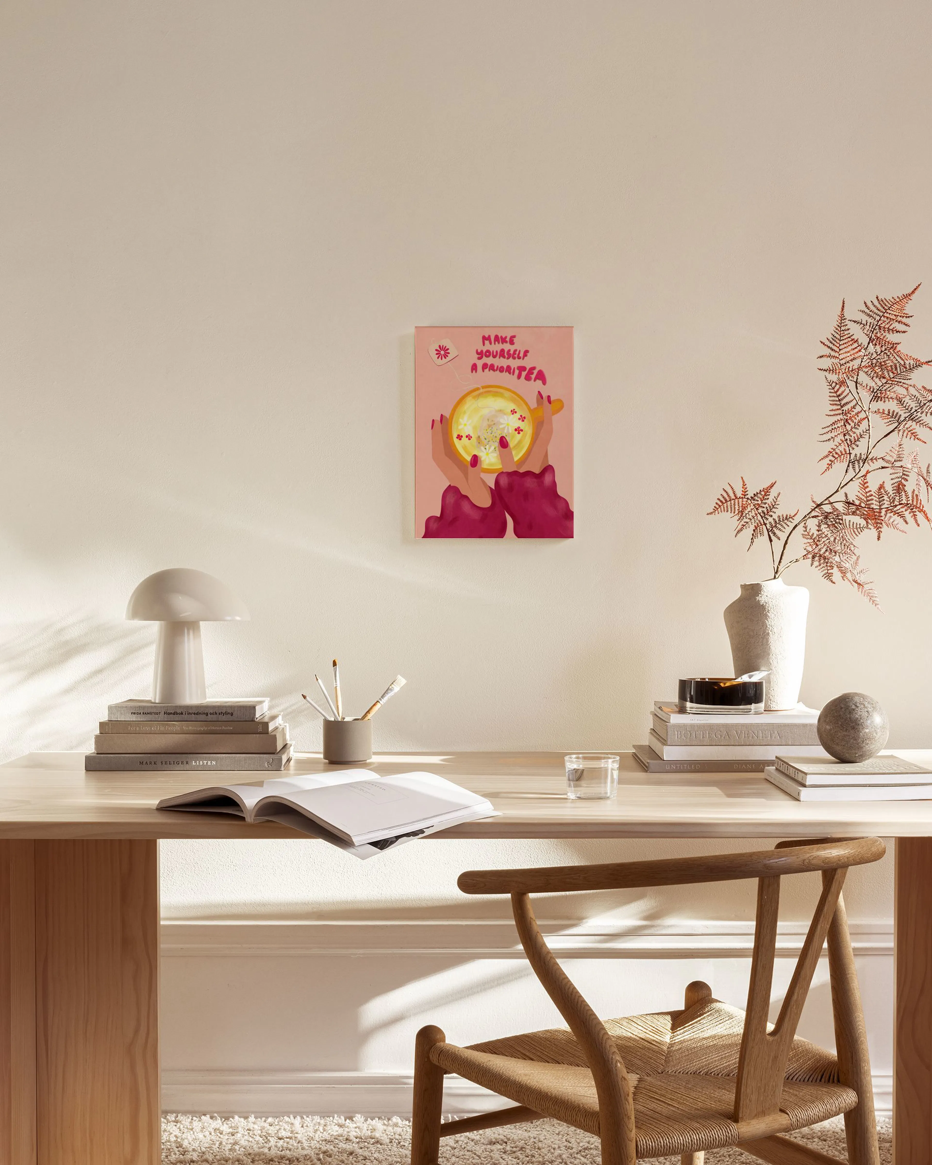 A vibrant pink canvas print with hands holding a yellow teacup, text Make Yourself a PrioriTEA, hanging in a modern living room.