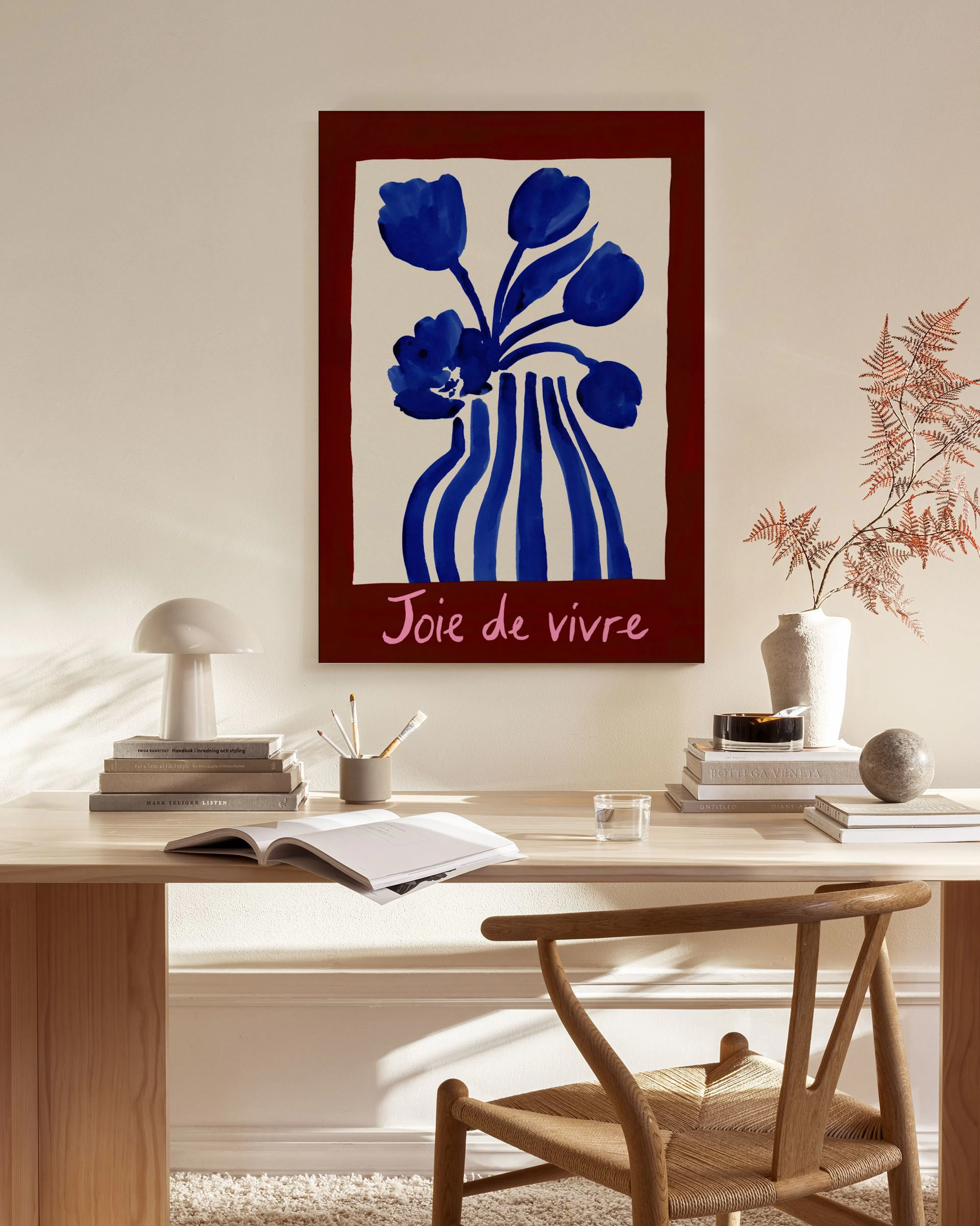 A canvas print of blue flowers in a striped vase on a red background with Joie de vivre, hanging in a natural, minimalist living