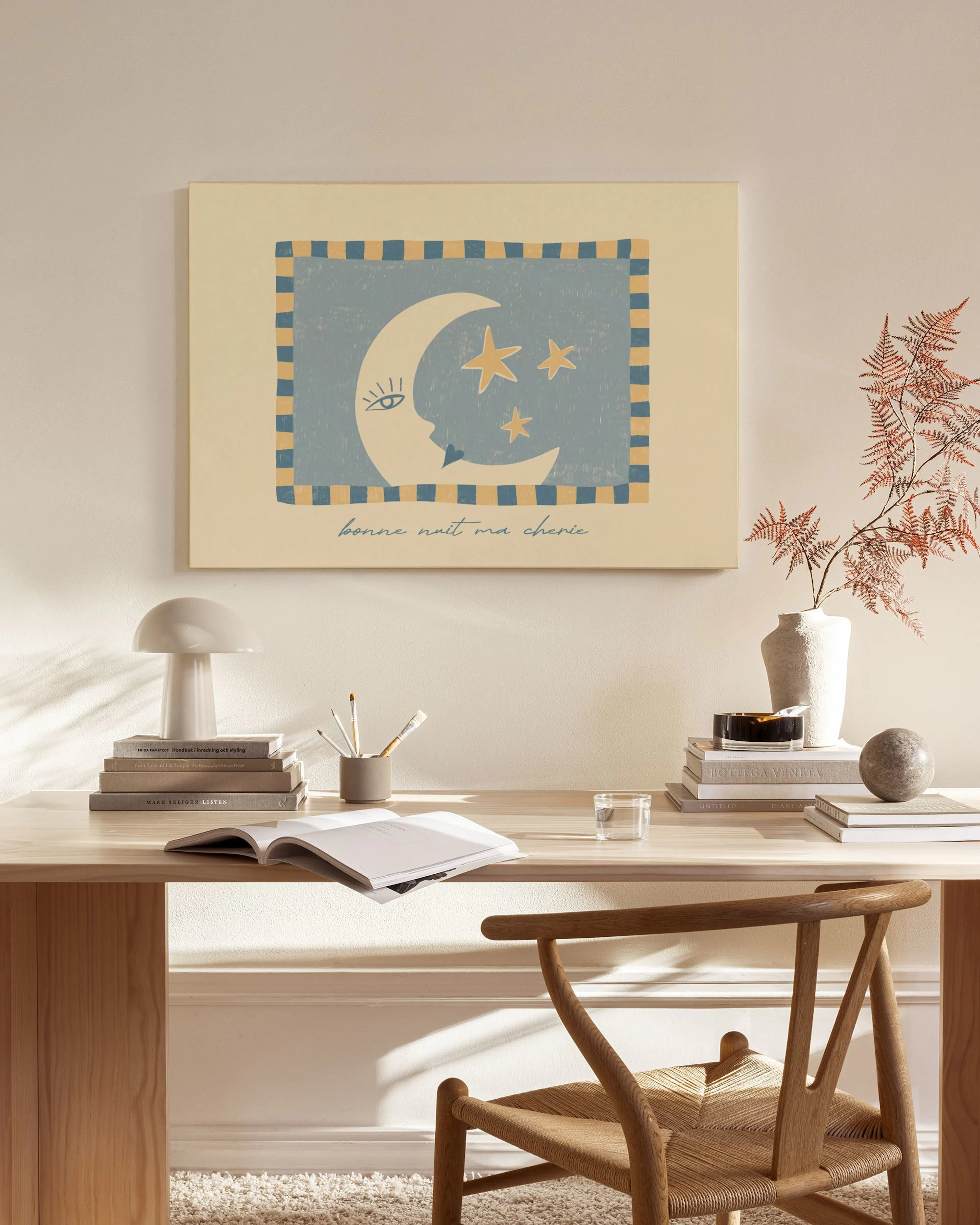 A canvas print of a crescent moon with stars on a blue and yellow patterned background, hanging in a minimalist living room.