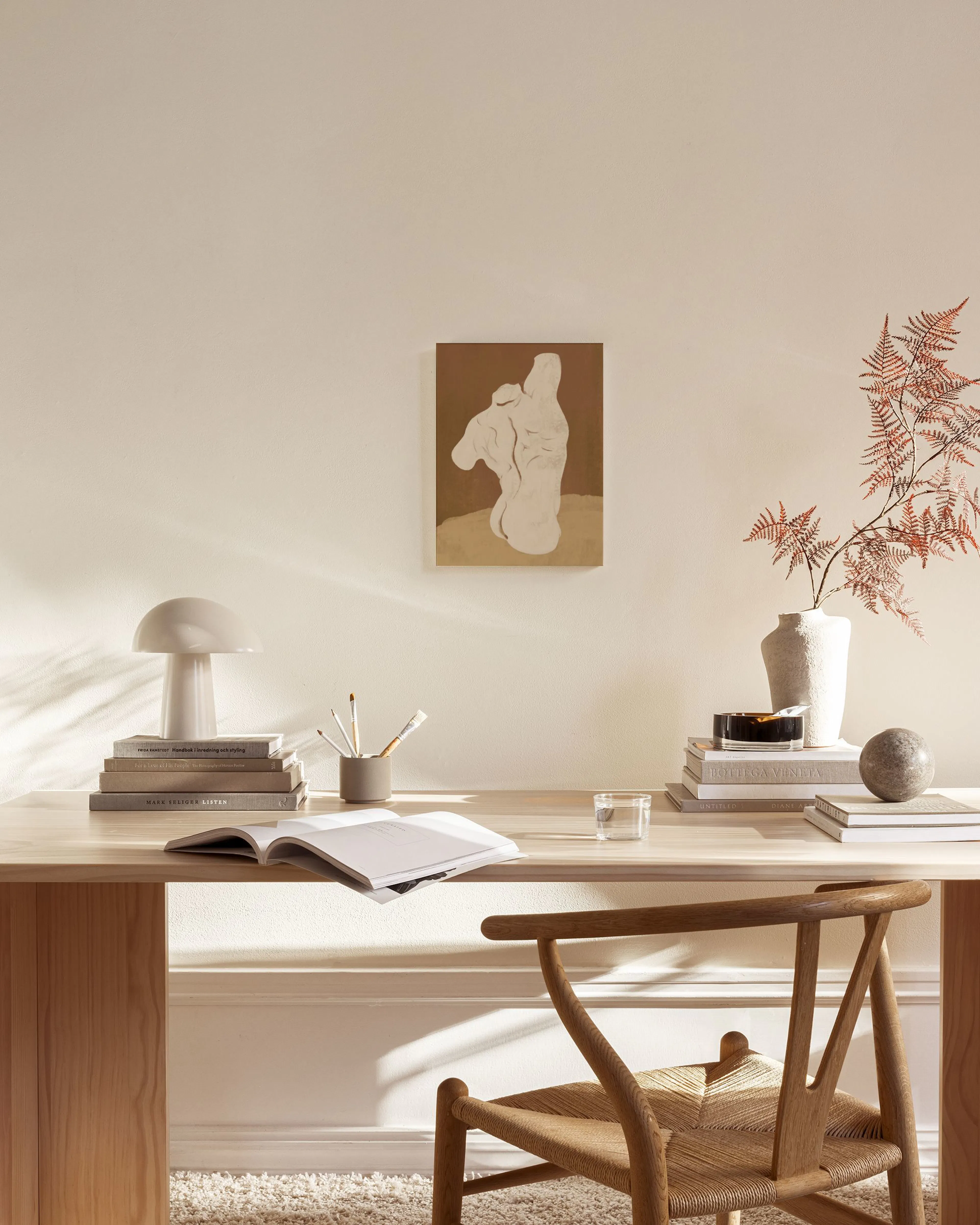 An abstract print featuring a light beige, figure-like shape on a brown and tan background, hanging above a console table in a m