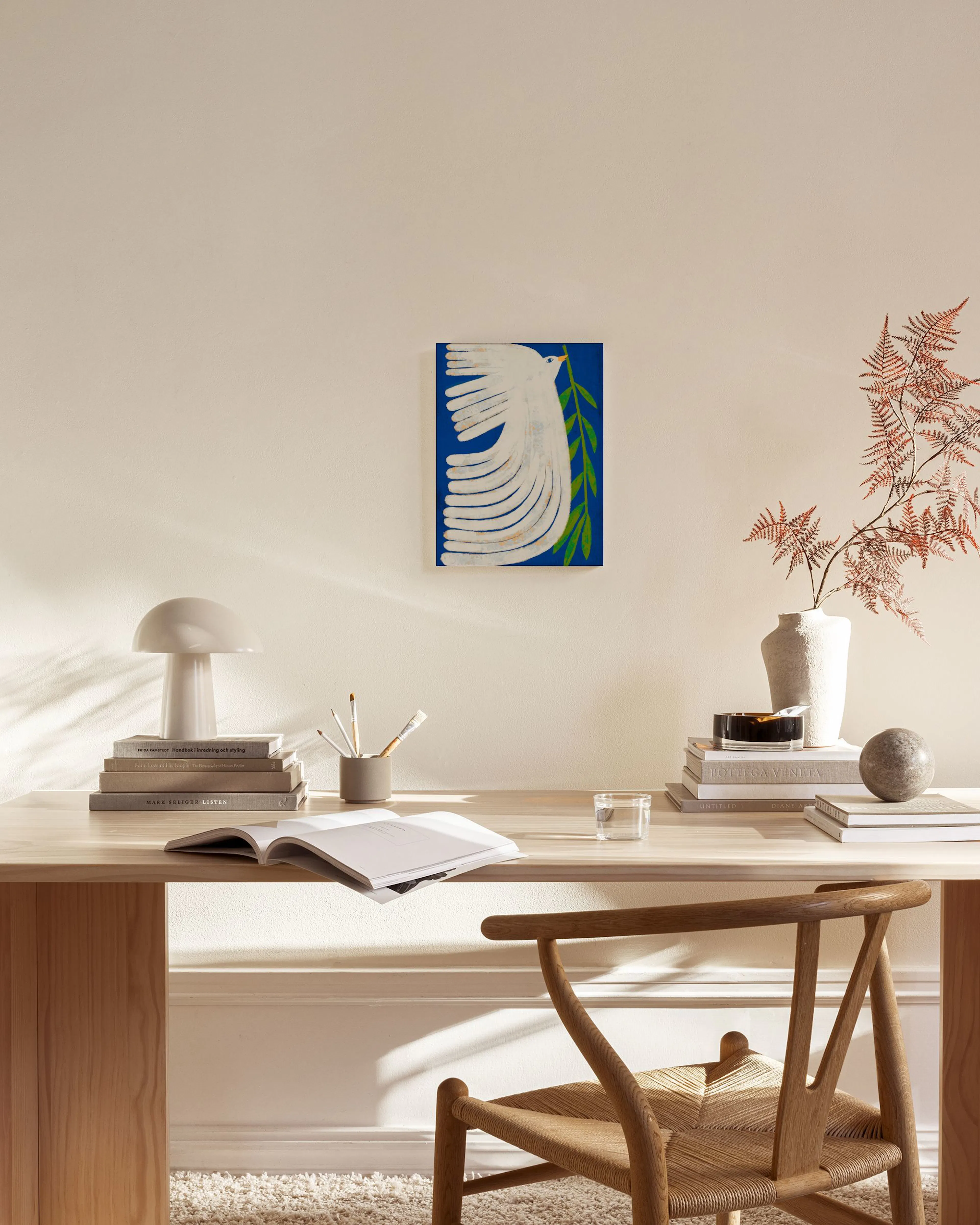 Canvas met een witte duif die een olijftak draagt op een blauwe achtergrond, hangend boven een houten dressoir in een lichte woo