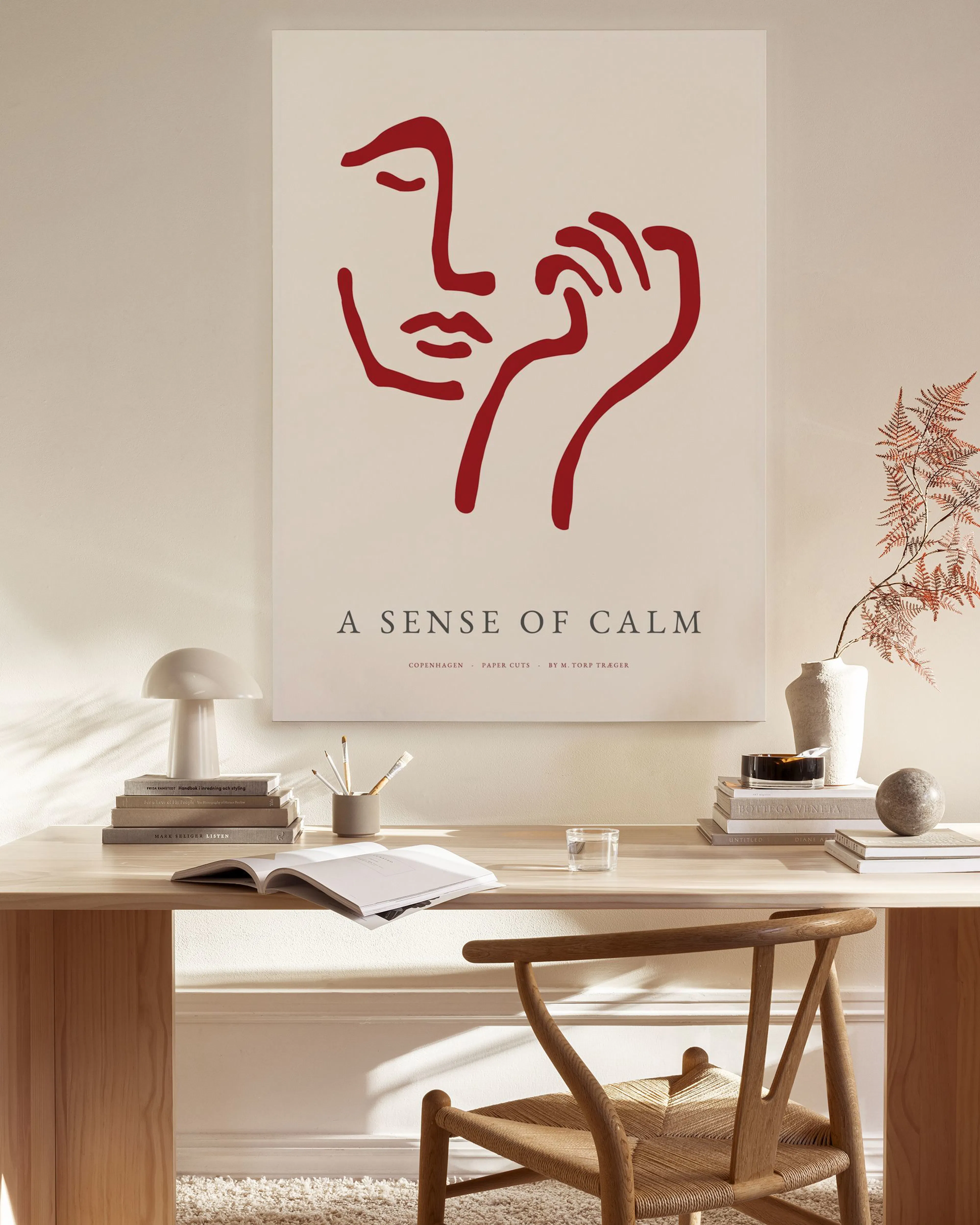 A red minimalist line art face with a hand, on a light background, hanging in a bright, modern living room.