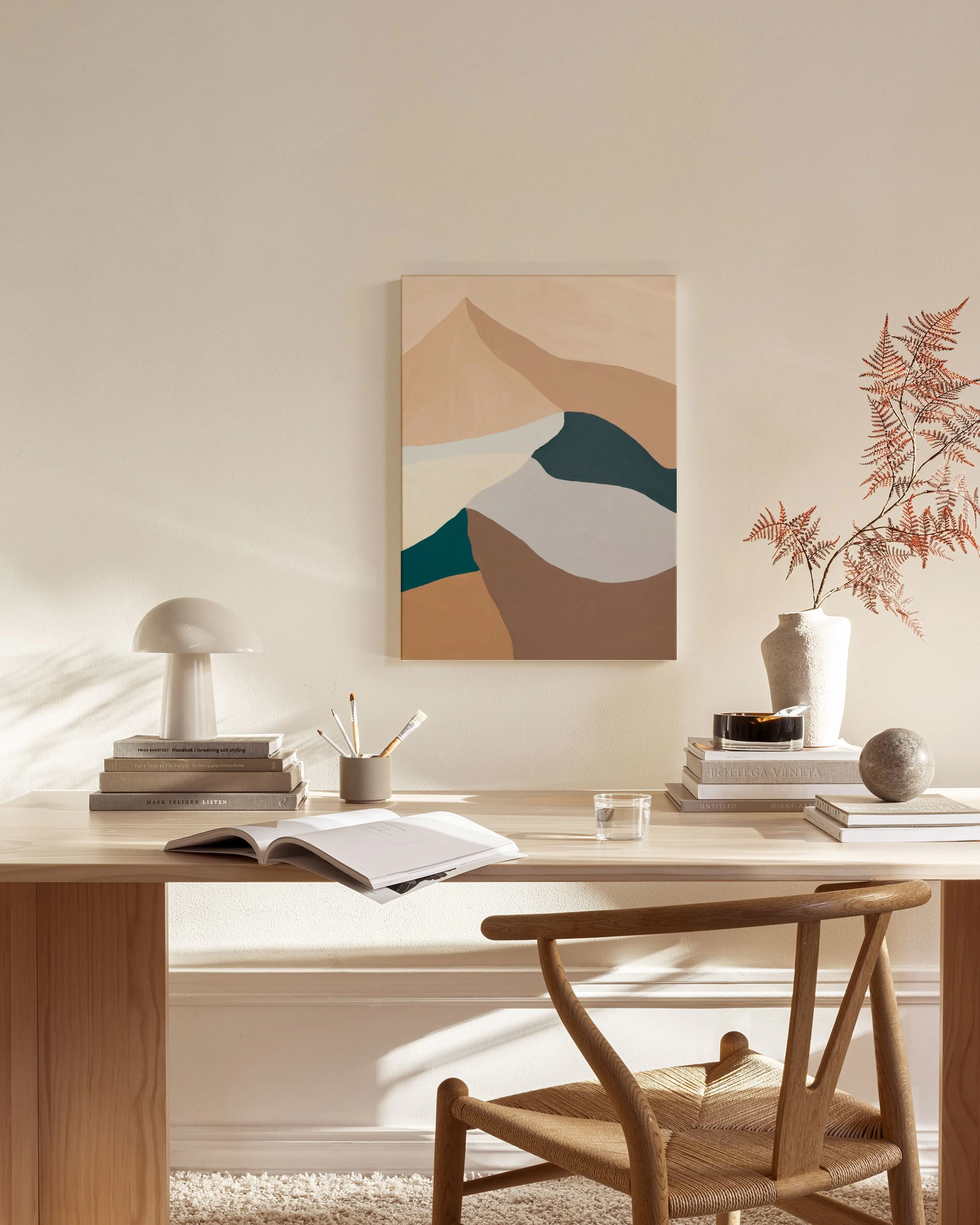 Lienzo abstracto de montañas y un río en tonos tierra, azules y grises, colgado en una sala de estar minimalista.