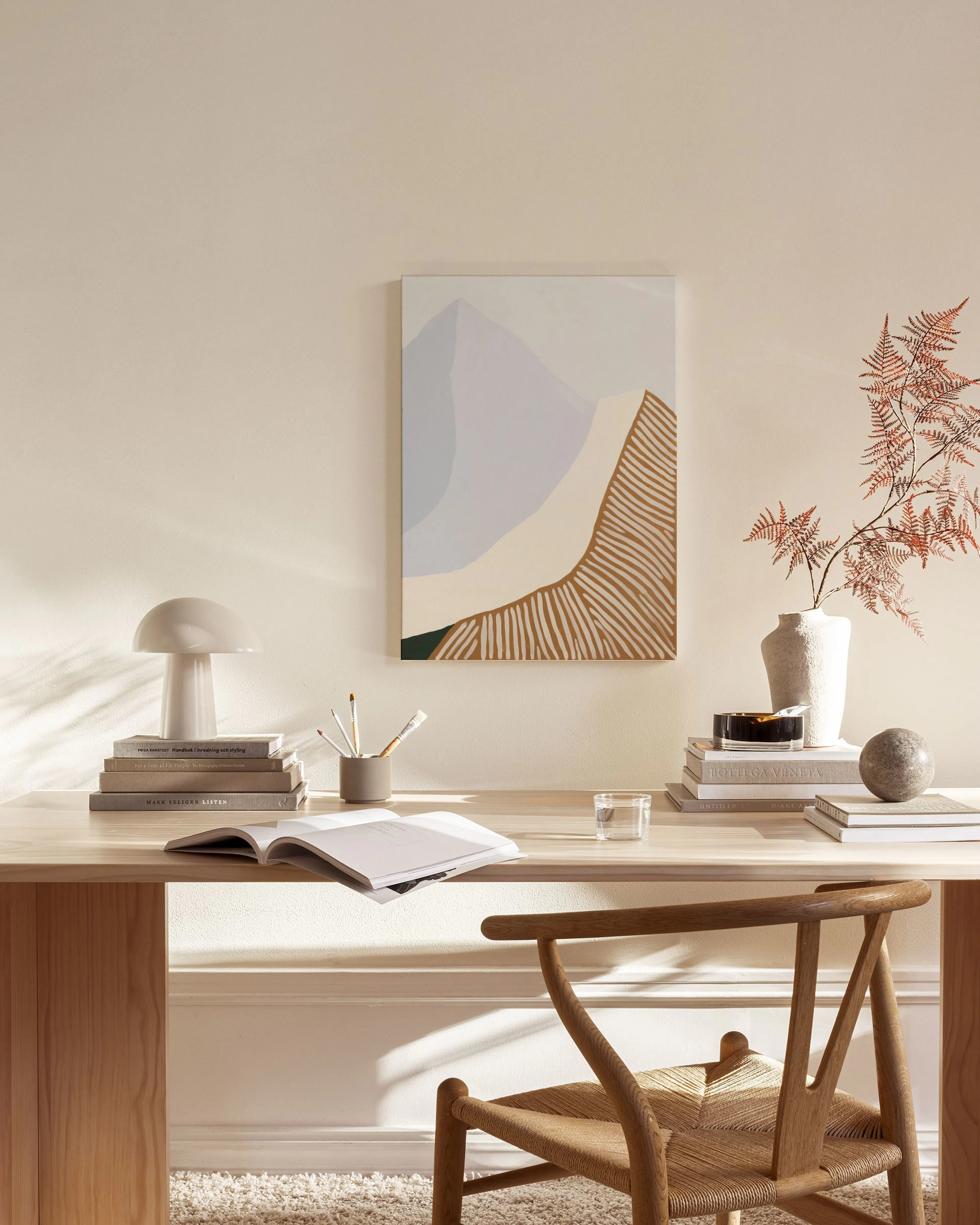 Canvas met berglandschap in lichtblauw, beige en bruine strepen, hangend boven een houten dressoir in een woonkamer.