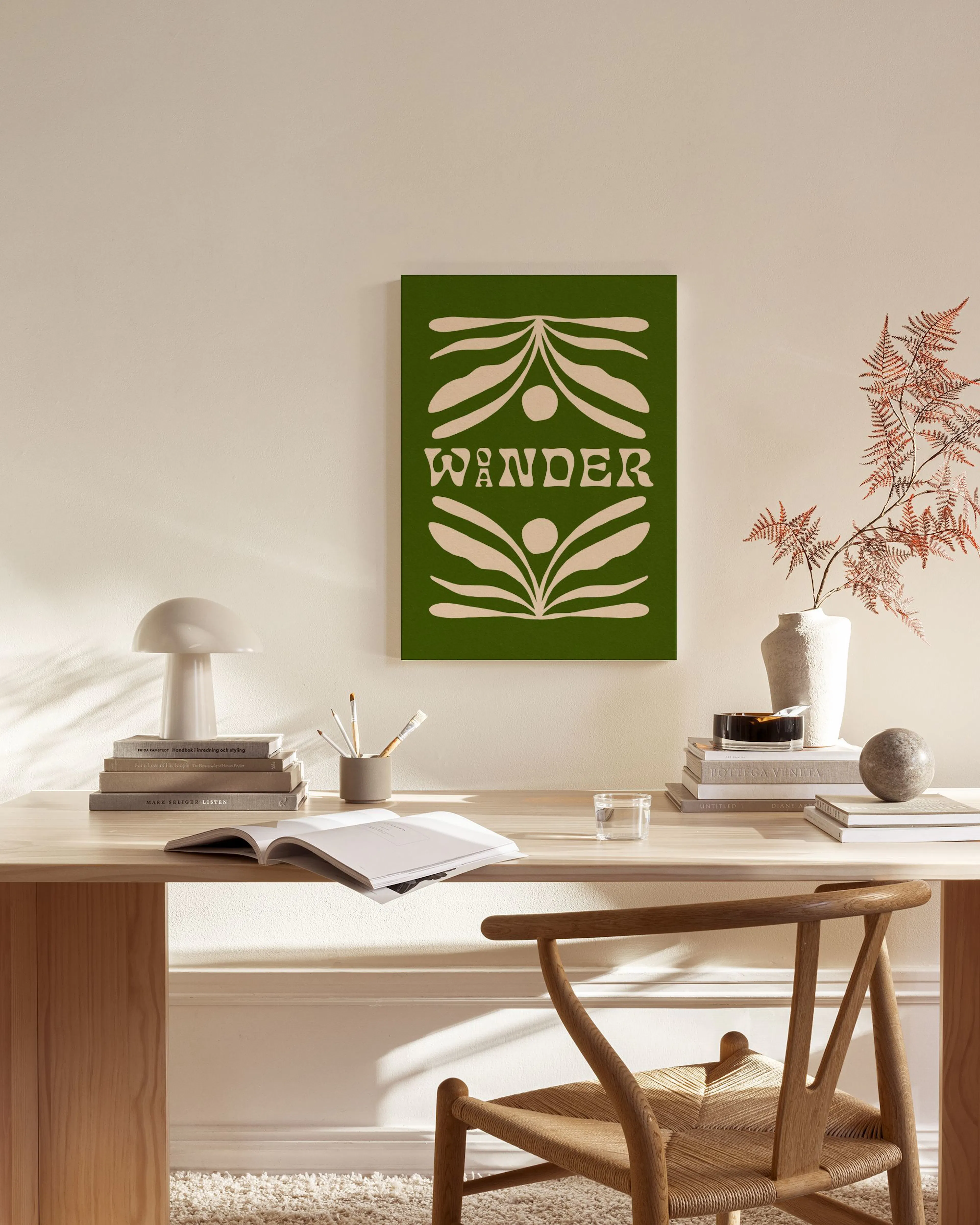 Grünes Leinwandbild mit cremefarbenen Blättern und dem Wort WANDER, hängt in einem modernen Wohnzimmer über einem Sideboard.