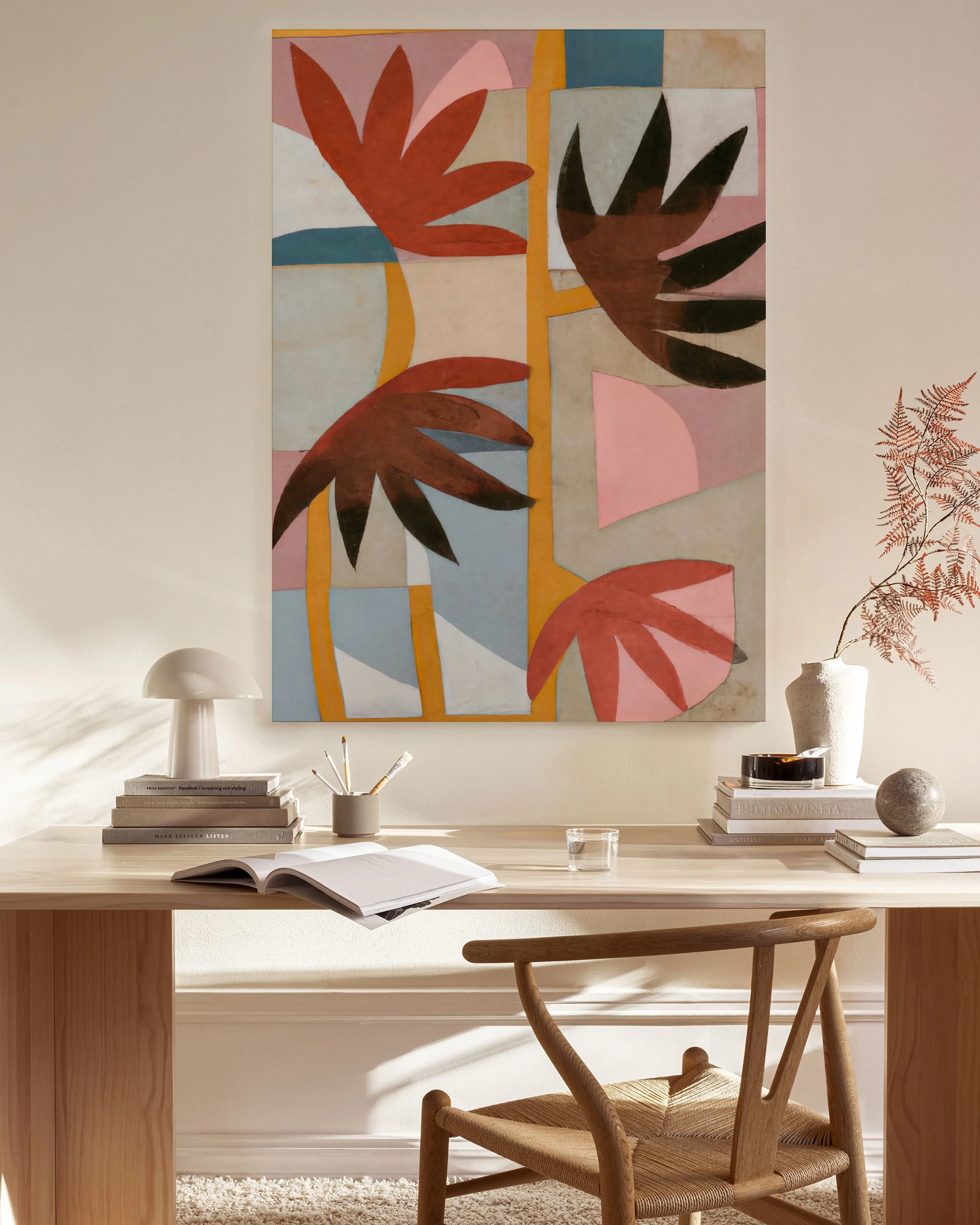 A canvas print with abstract flat shapes of red, black, and pink leaves on a blue and beige background, hanging in a minimalist 