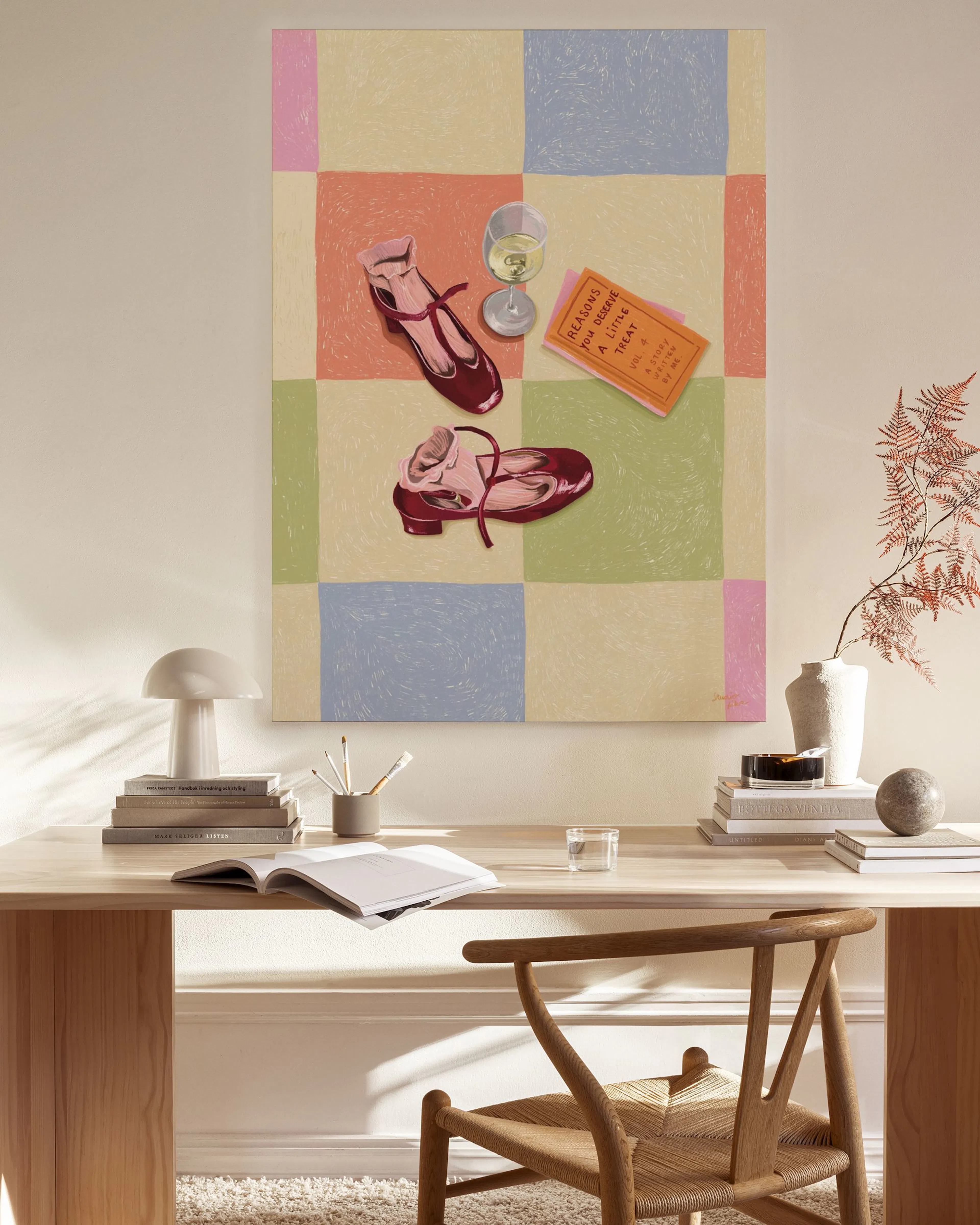 Lienzo con zapatos rojos, copa de vino y libro sobre cuadros pastel, colgado en una sala moderna.
