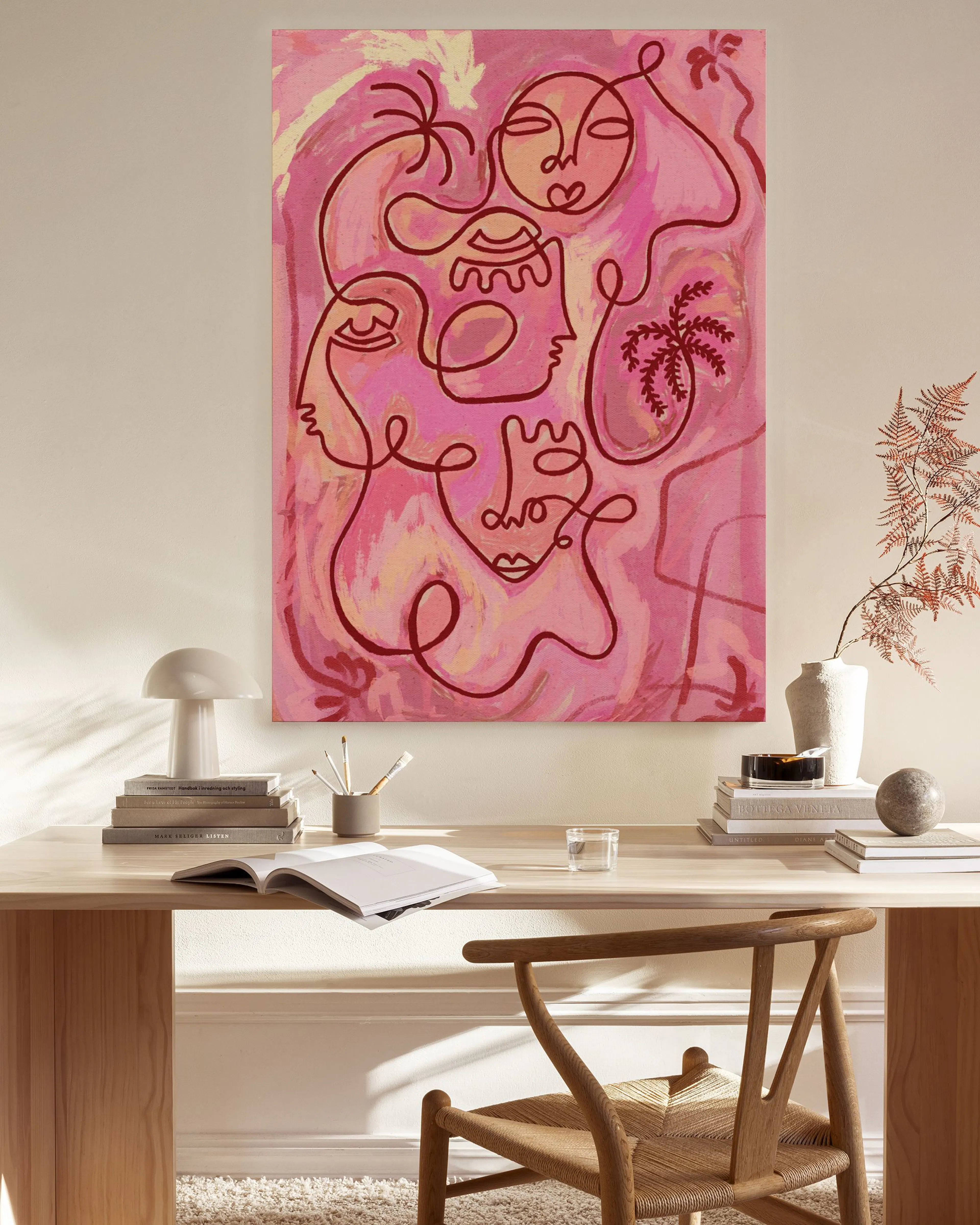 Pink line art canvas print with abstract faces and palm trees, hanging above a light timber console table in a minimalist living