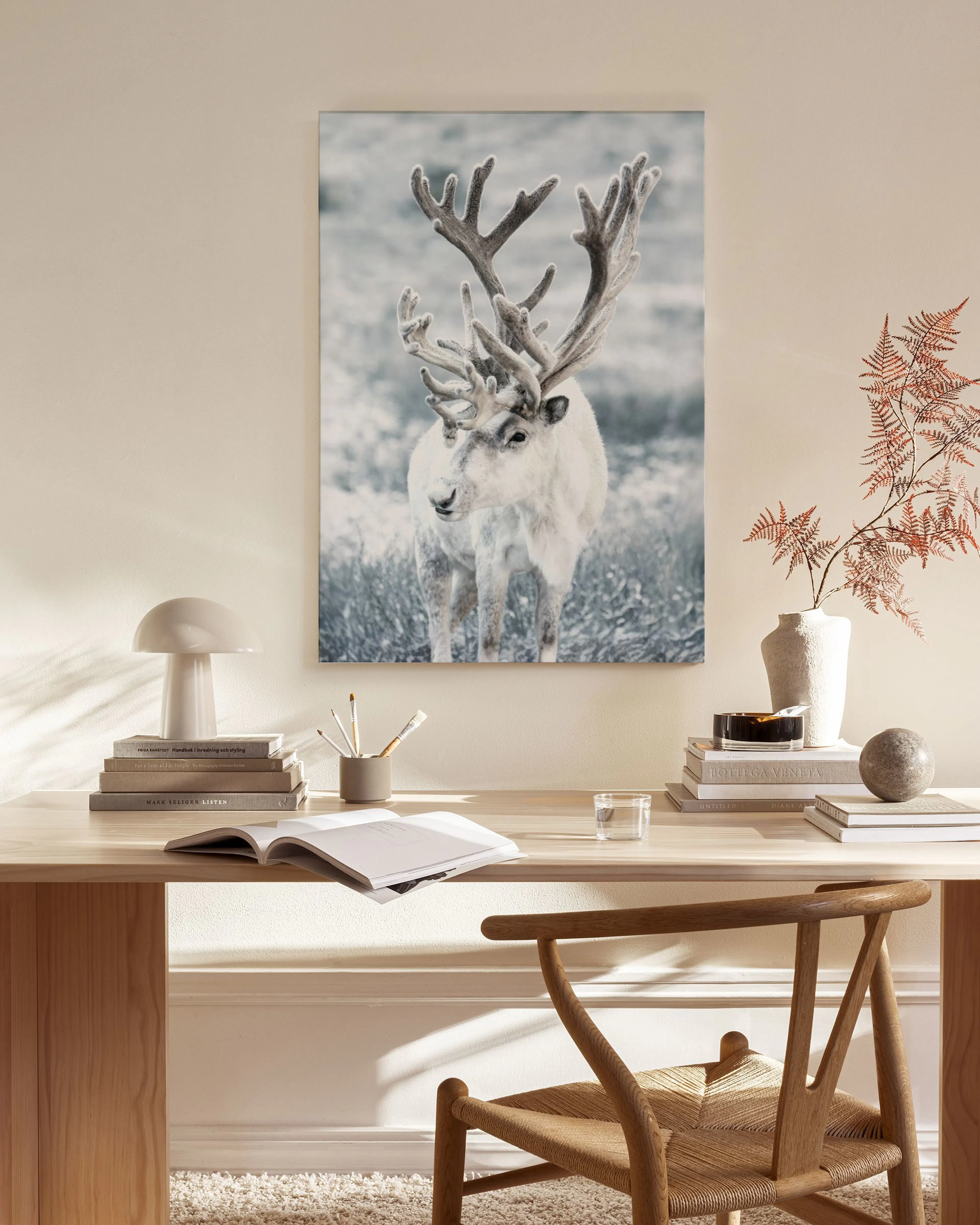 A canvas print of a white reindeer in a winter landscape, hanging above a wooden cabinet in a modern living room.