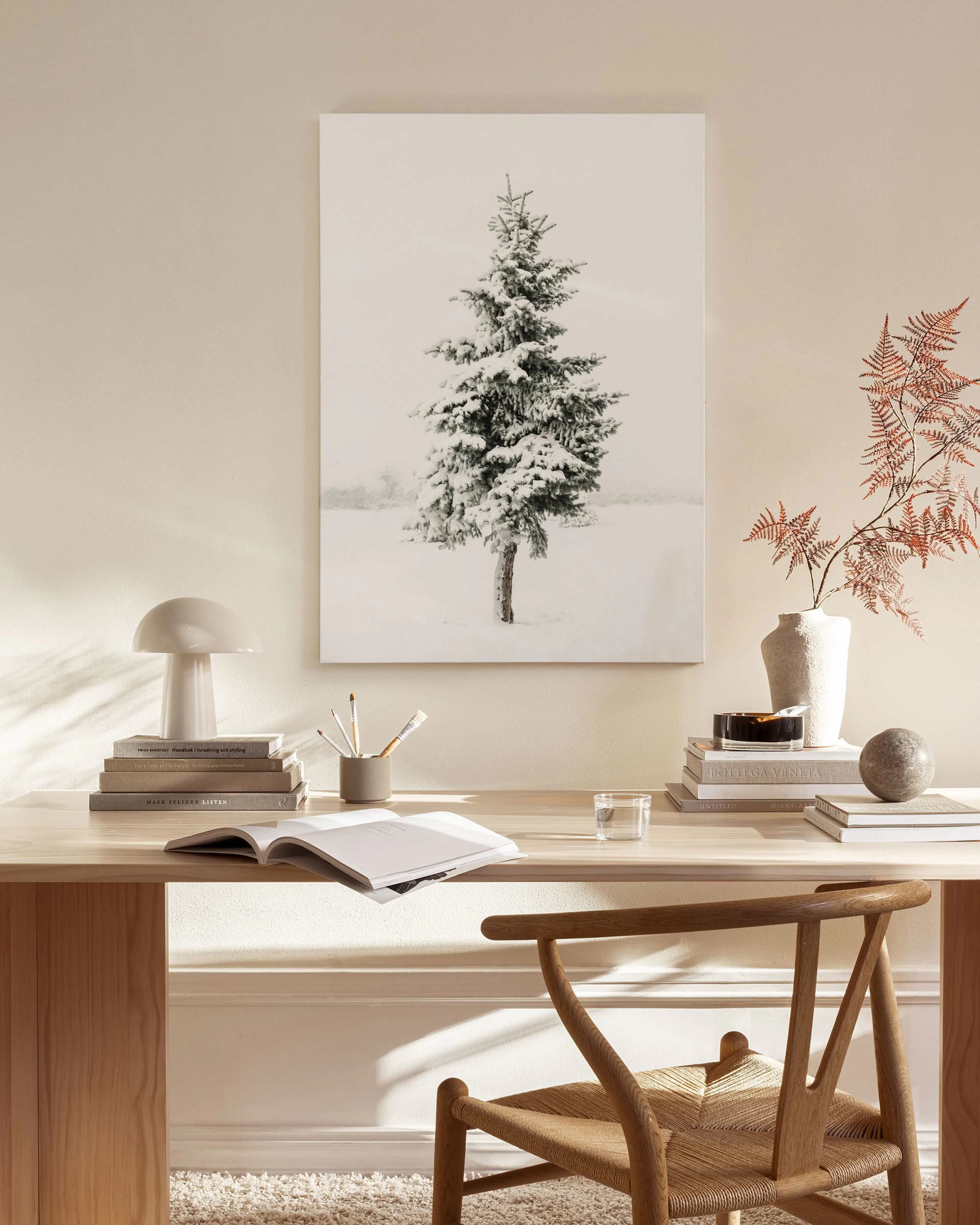 Canvas van een groene dennenboom bedekt met sneeuw, hangend in een lichte woonkamer boven een houten dressoir.