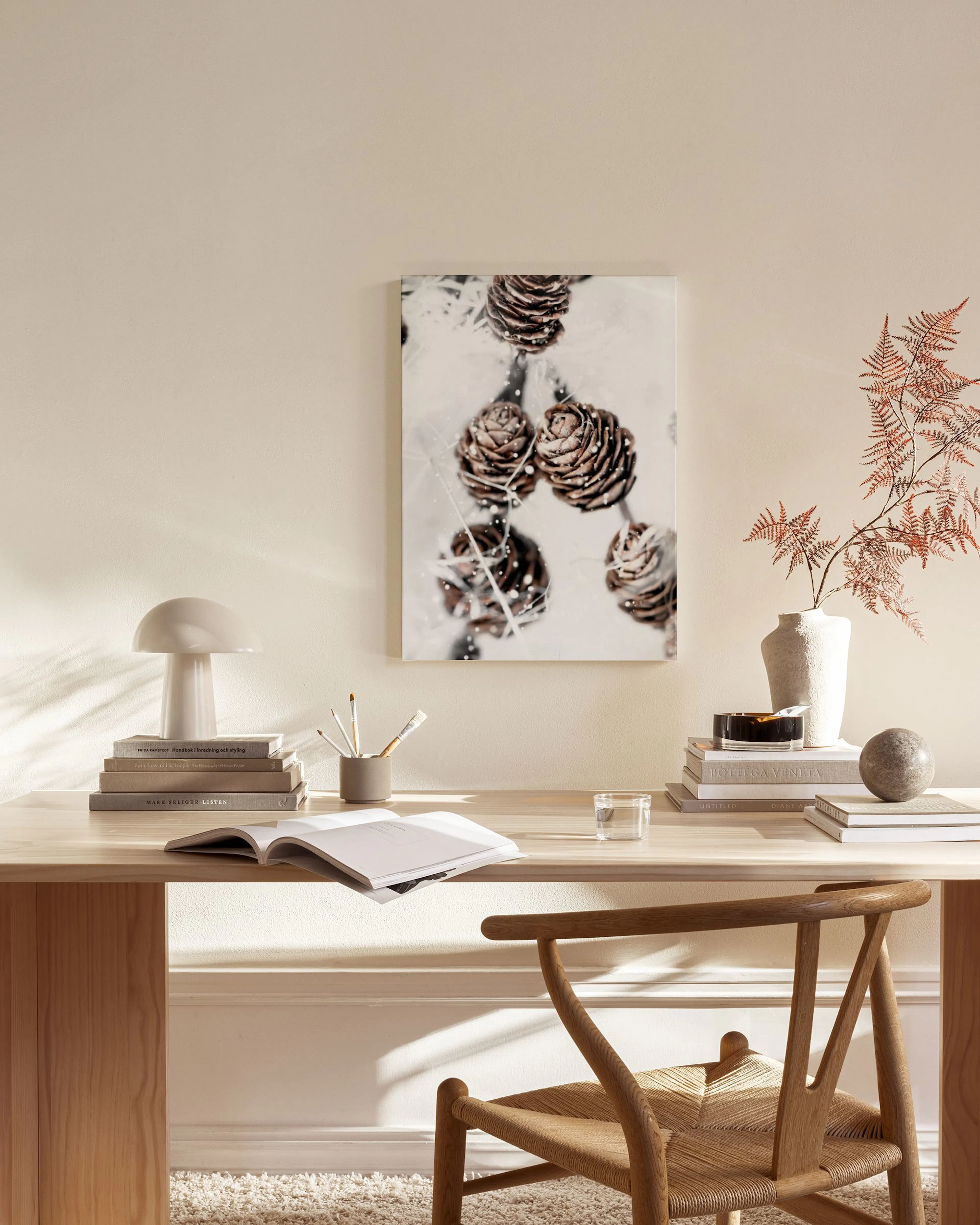A canvas print of brown pine cones covered in snow, hanging on a light wall in a minimalist living room.