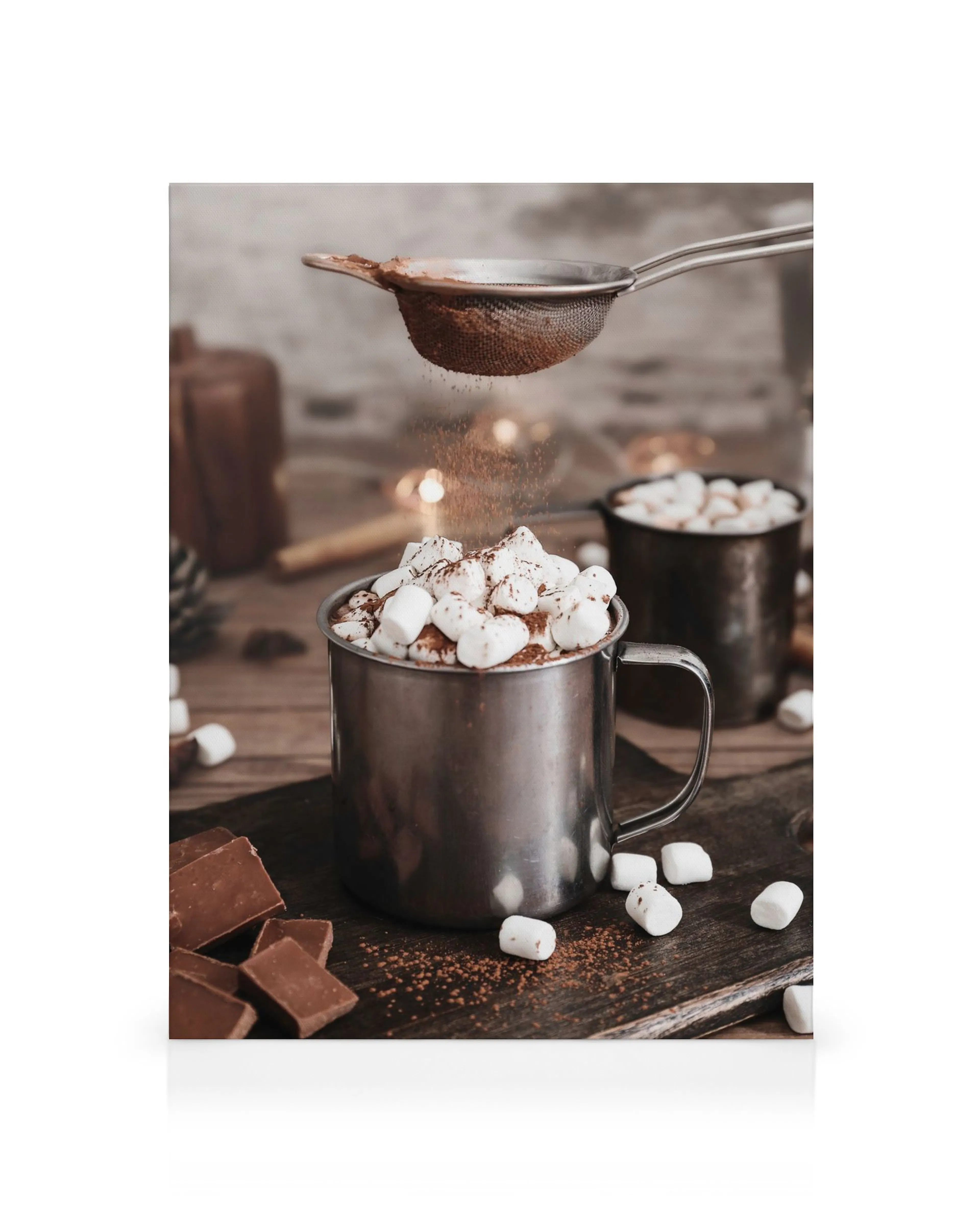 Varm chokolade i stålkrus med skumfiduser, drysset med kakao fra si, på træbaggrund.