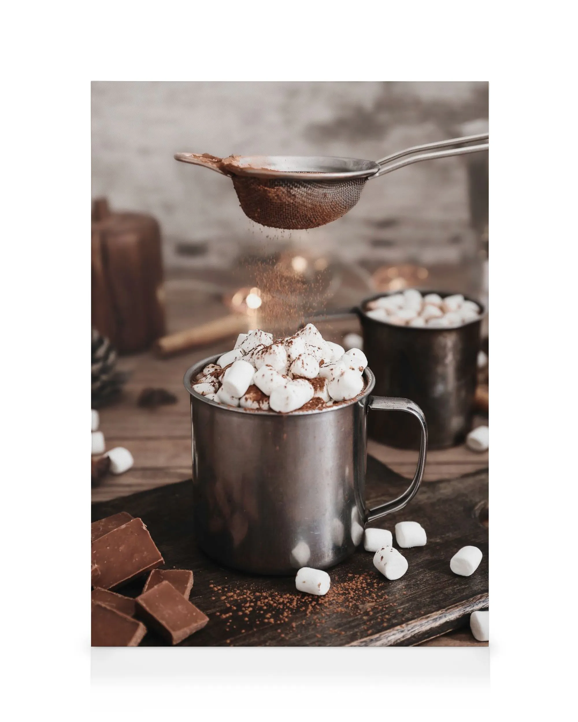 Varm chokolade i stålkrus med skumfiduser, drysset med kakao fra si, på træbaggrund.