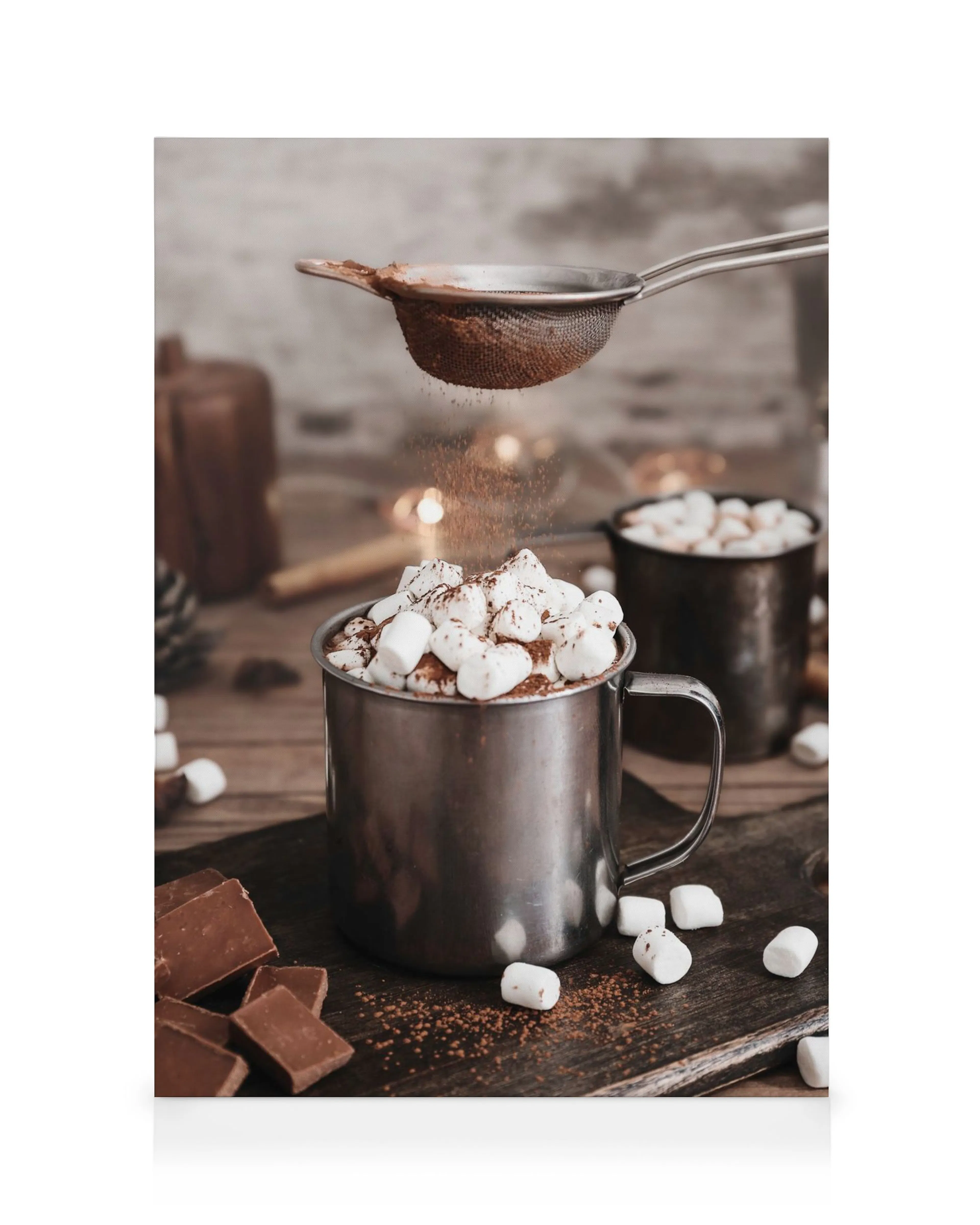 Varm chokolade i stålkrus med skumfiduser, drysset med kakao fra si, på træbaggrund.