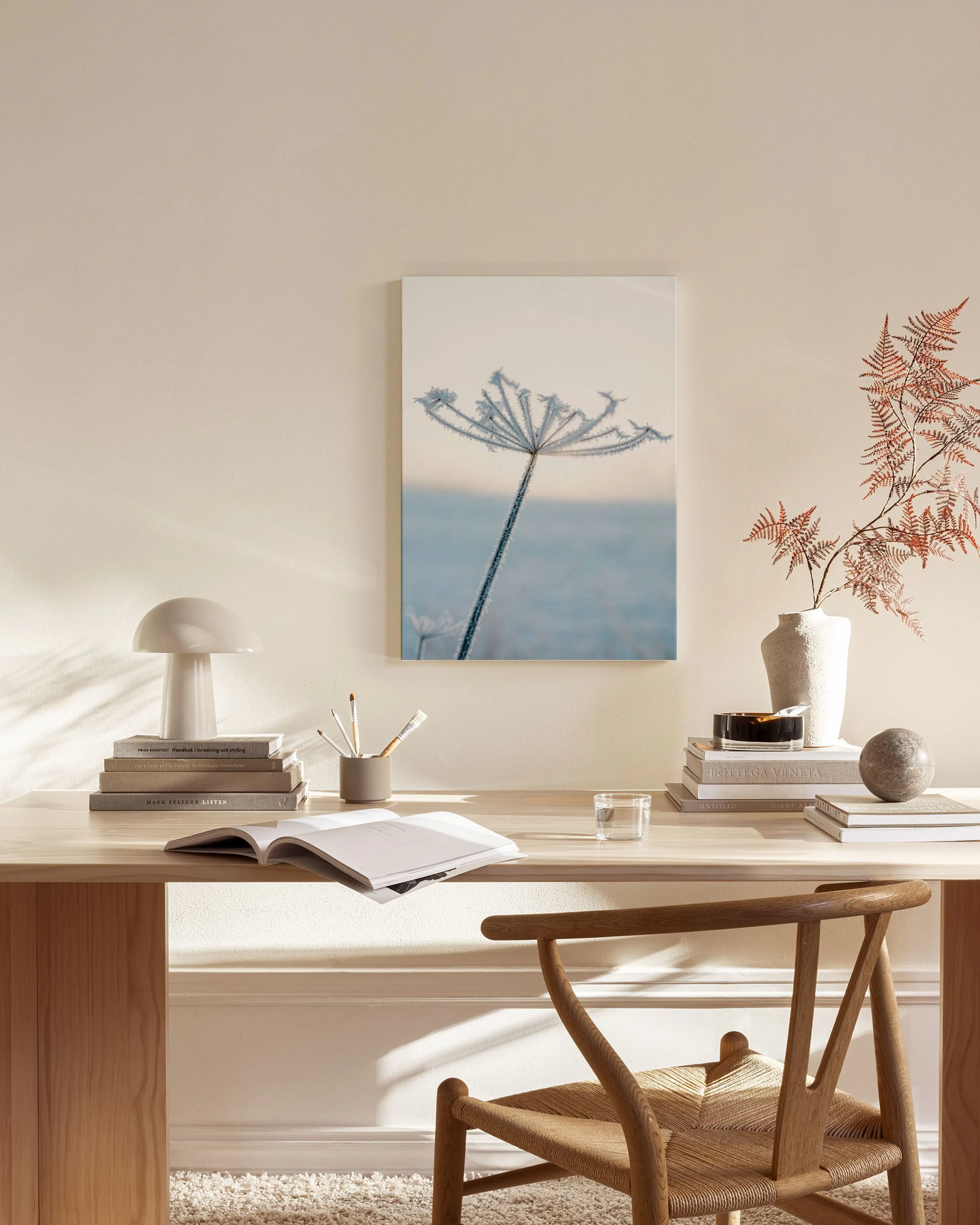 A canvas print of a frosted plant against a soft blue and white sky, hanging in a minimalist living room.