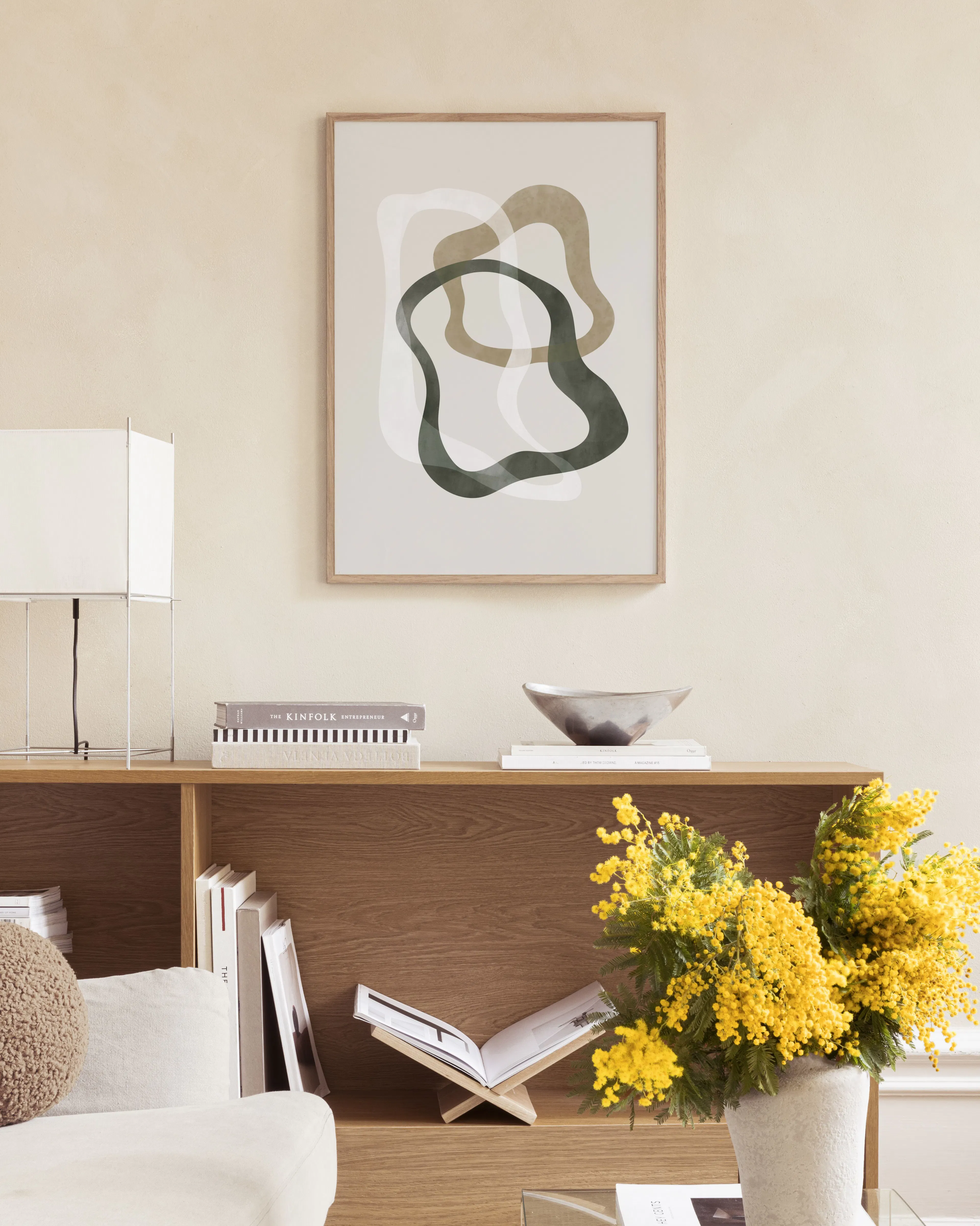 Abstract print with overlapping organic shapes in green, beige, and white, hanging above a marble side table with vases.