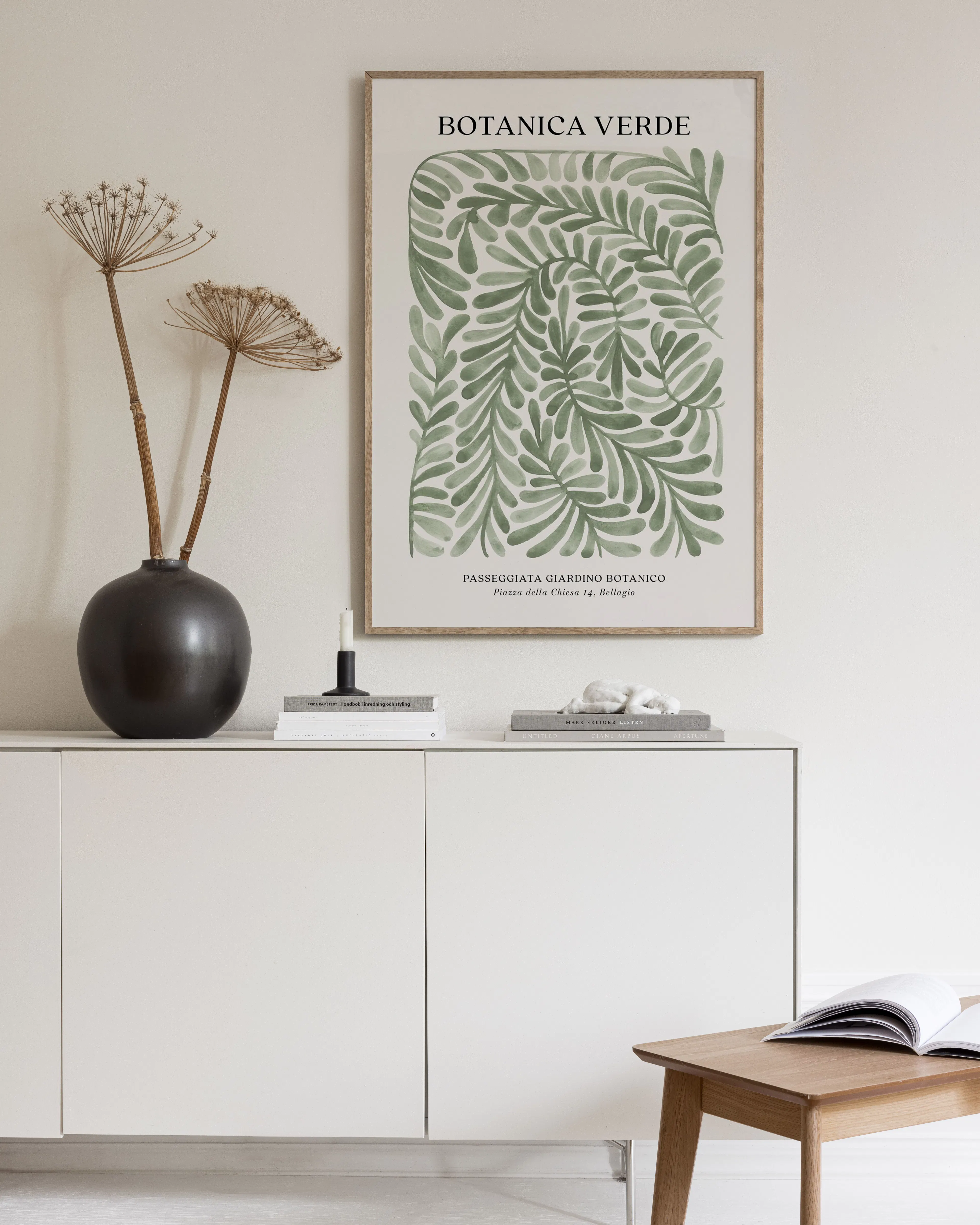 A botanical print with repeating green leaf patterns, hanging above a white cabinet in a bright room.