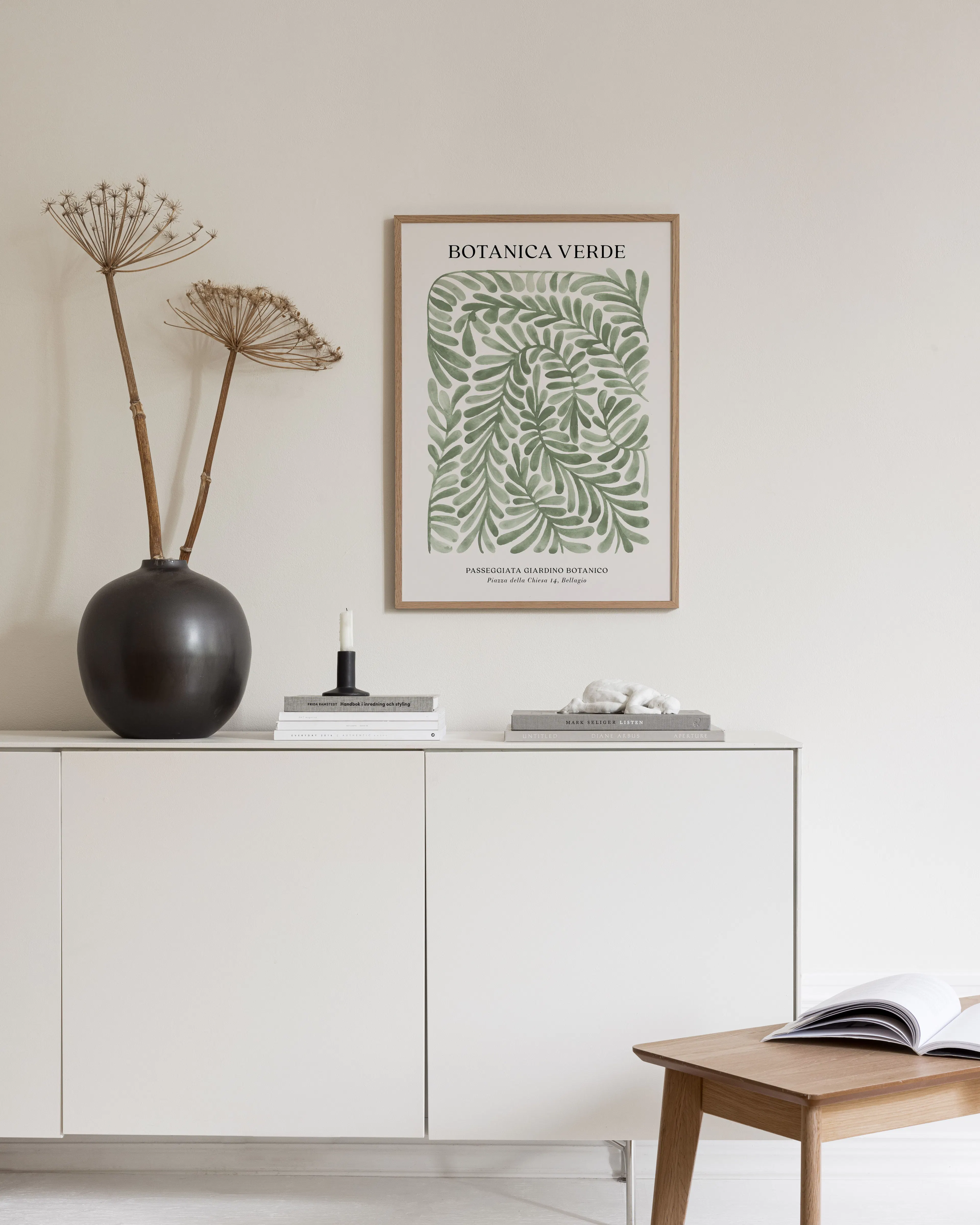 Botanica Verde botanical print with green leaves, displayed above a white console table with a black vase and books.