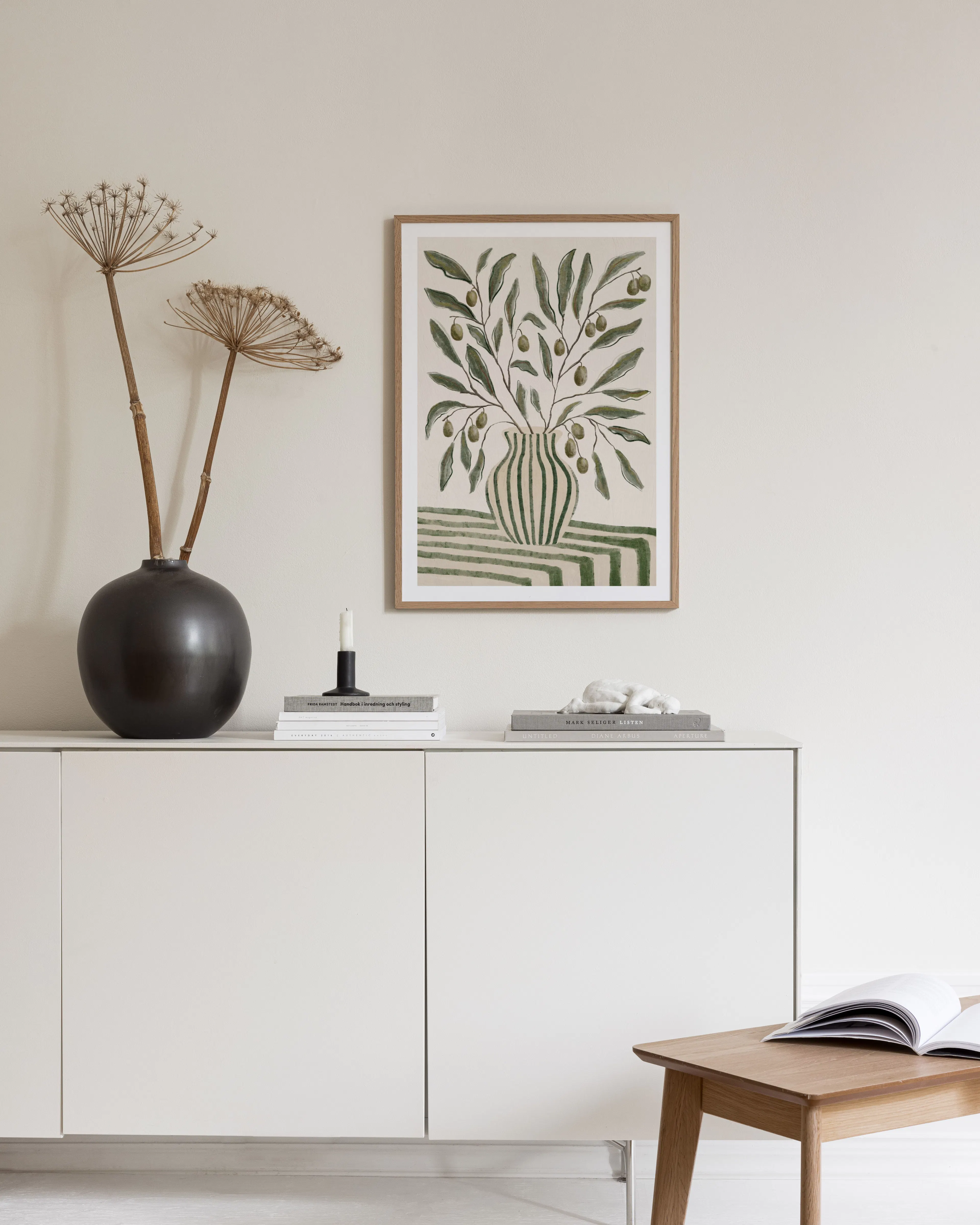Affiche dun bouquet dolivier dans un vase rayé vert, accrochée au-dessus dun bureau en bois clair avec une chaise bouclée.