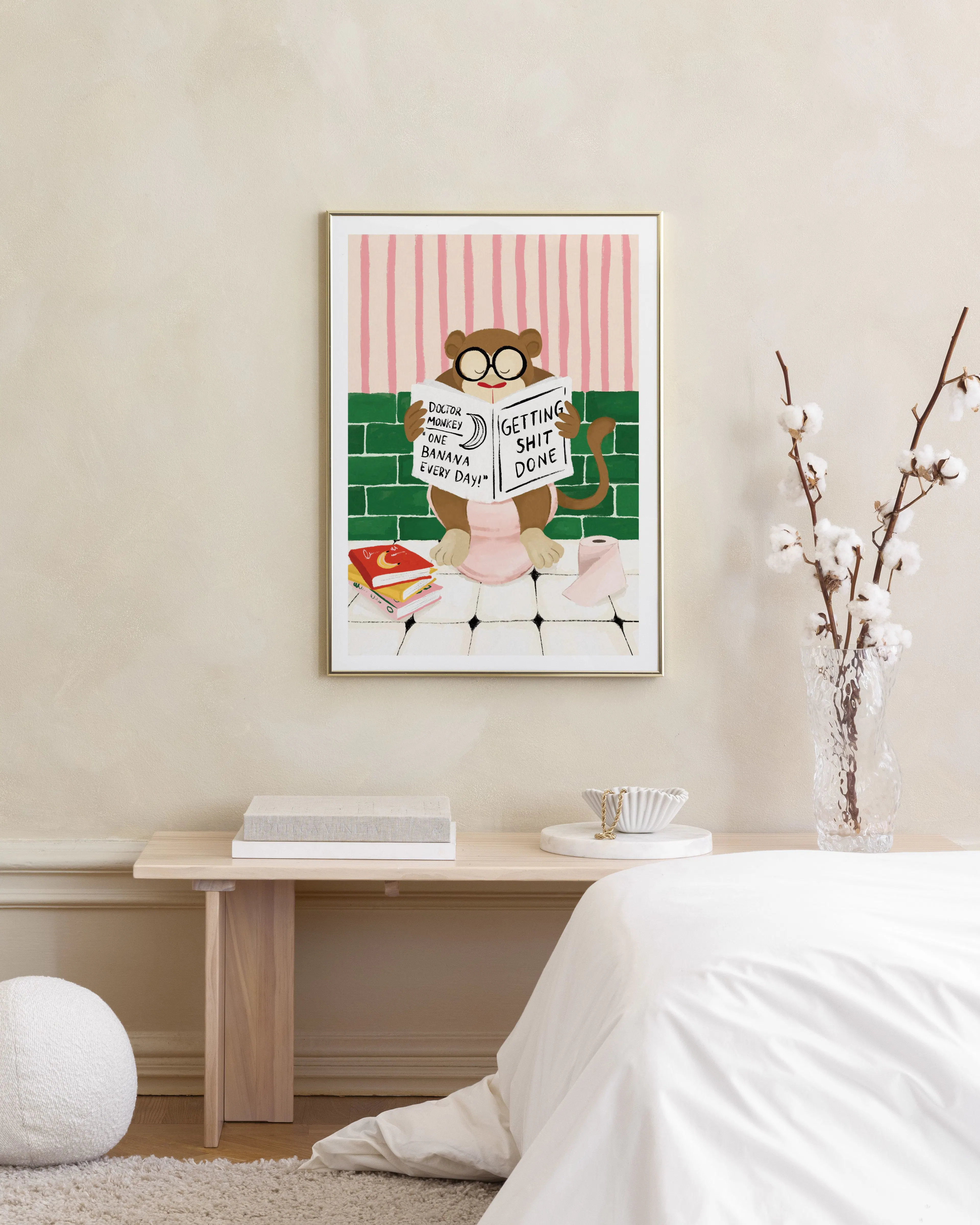 A humorous print of a monkey wearing glasses, reading a newspaper on a toilet, displayed above a wooden bench in a bedroom.