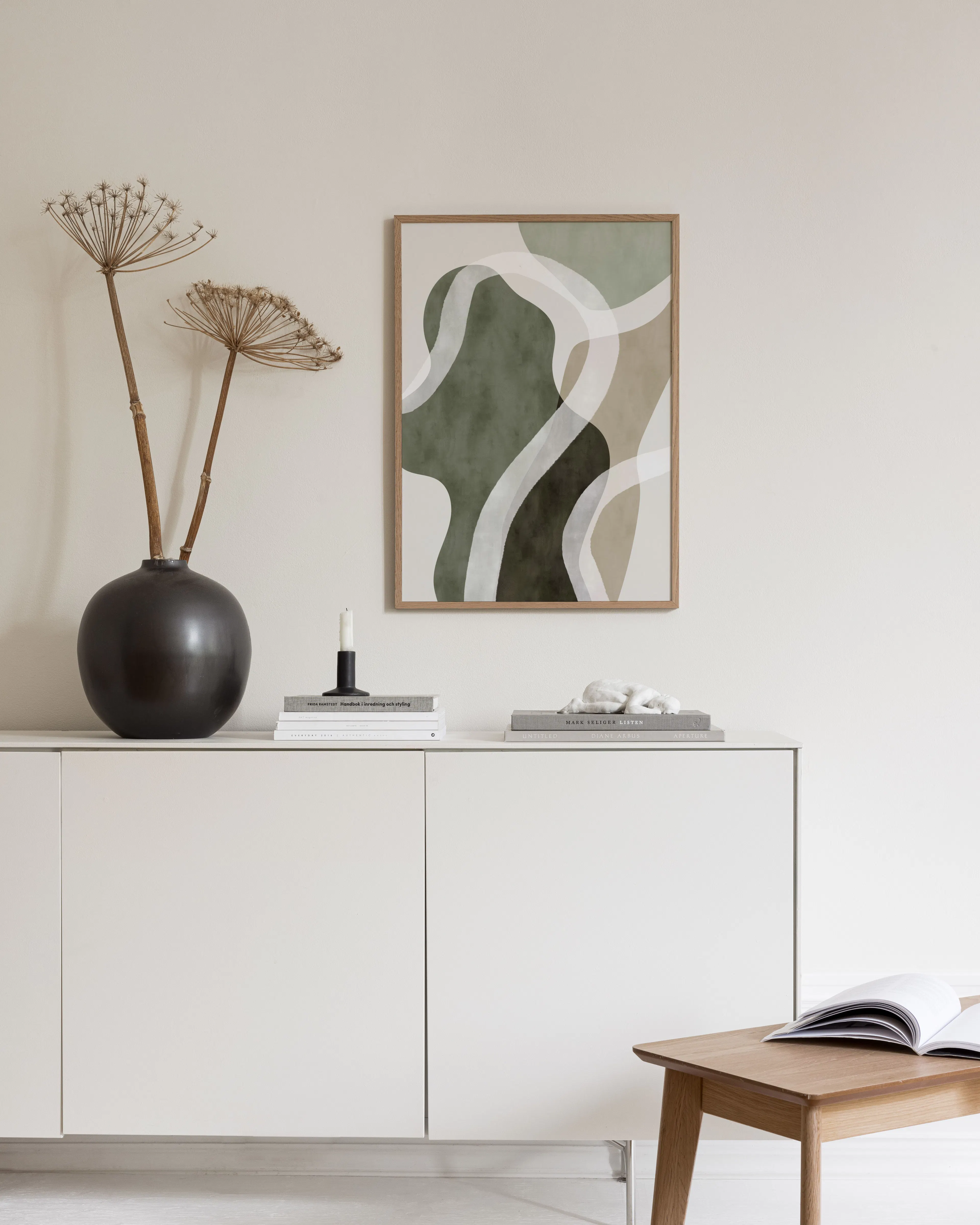 Poster met abstracte vormen in groen, beige en donkerbruin, met witte golvende lijnen, hangend in een moderne kamer met lamp en 