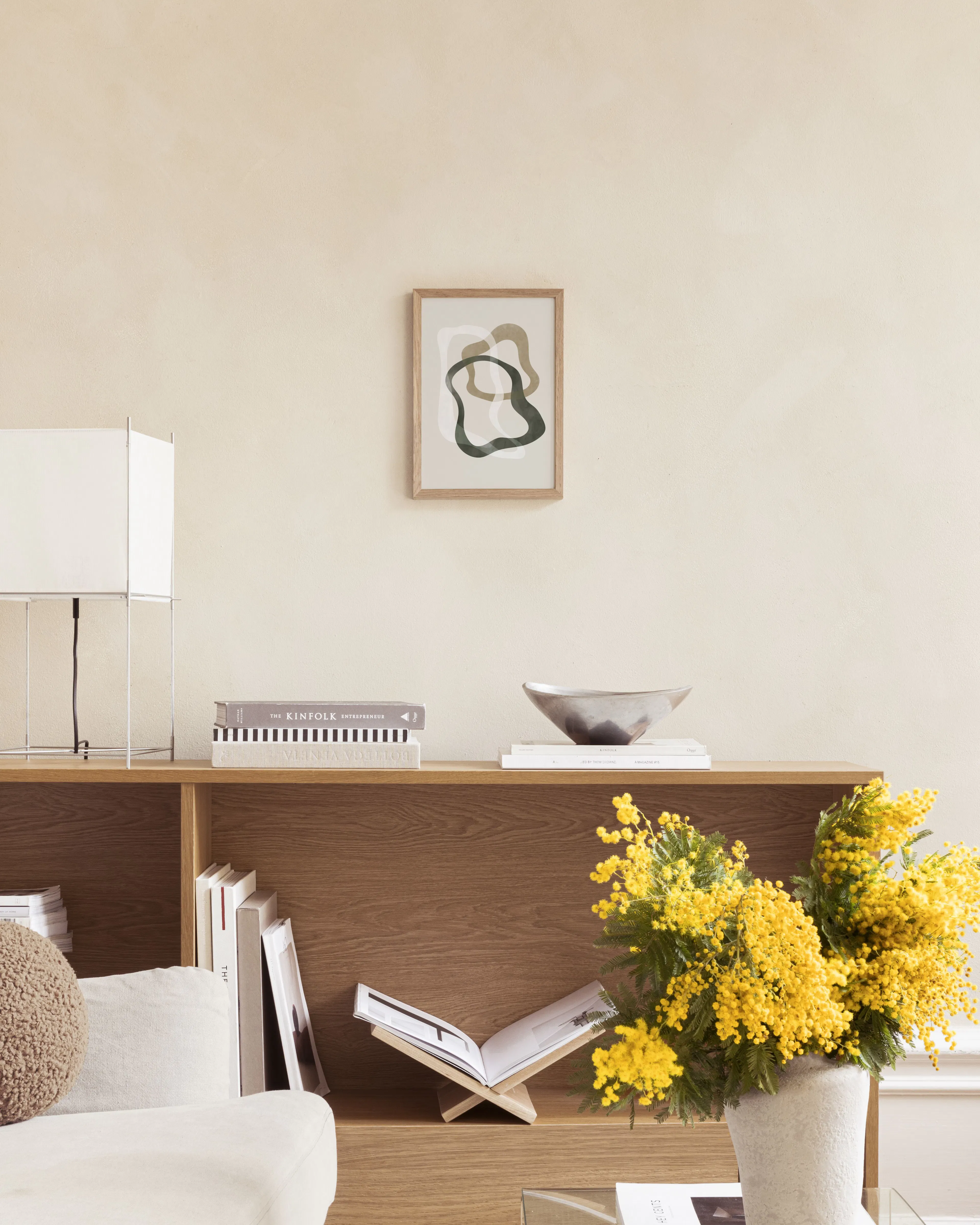 Poster mit organischen Formen in Grün, Beige und Weiß, hängend über einem Beistelltisch mit Vasen und Büchern.