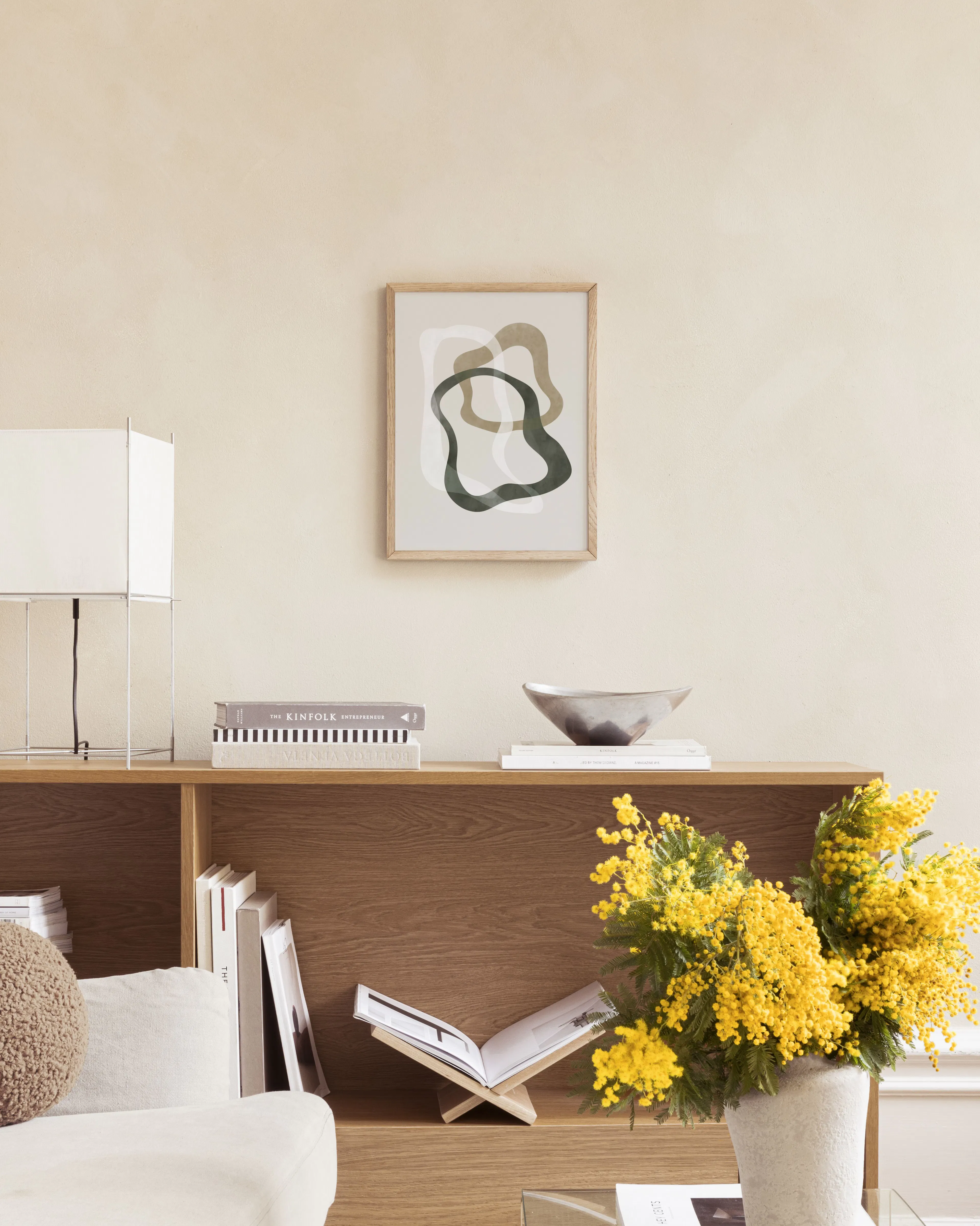 Poster met abstracte organische vormen in groen, bruin en wit op een lichtroze achtergrond, hangend boven een marmeren bijzettaf