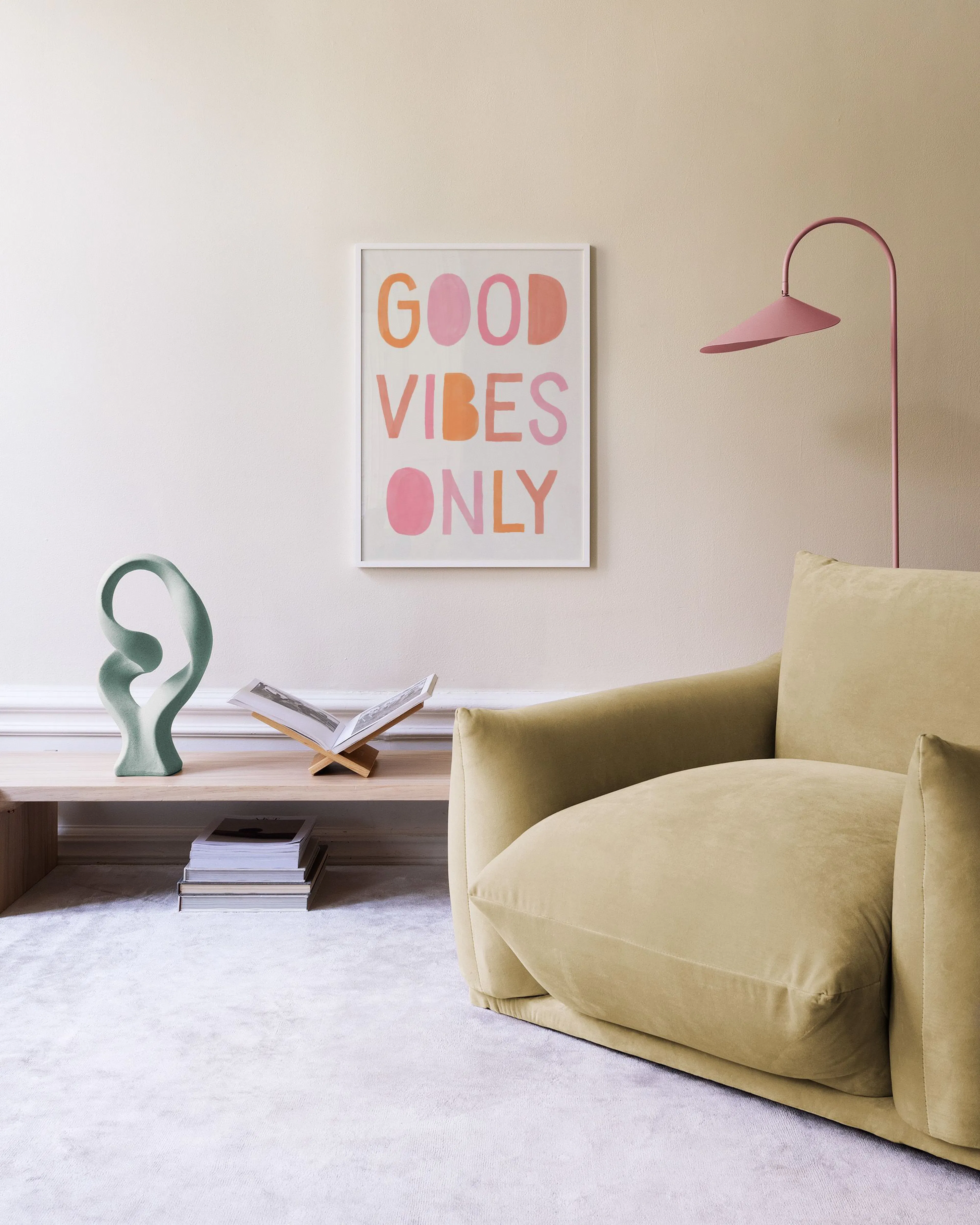 Plakat med teksten GOOD VIBES ONLY i rosa og oransje bokstaver, henger over en hvit kommode med bøker og en lampe.