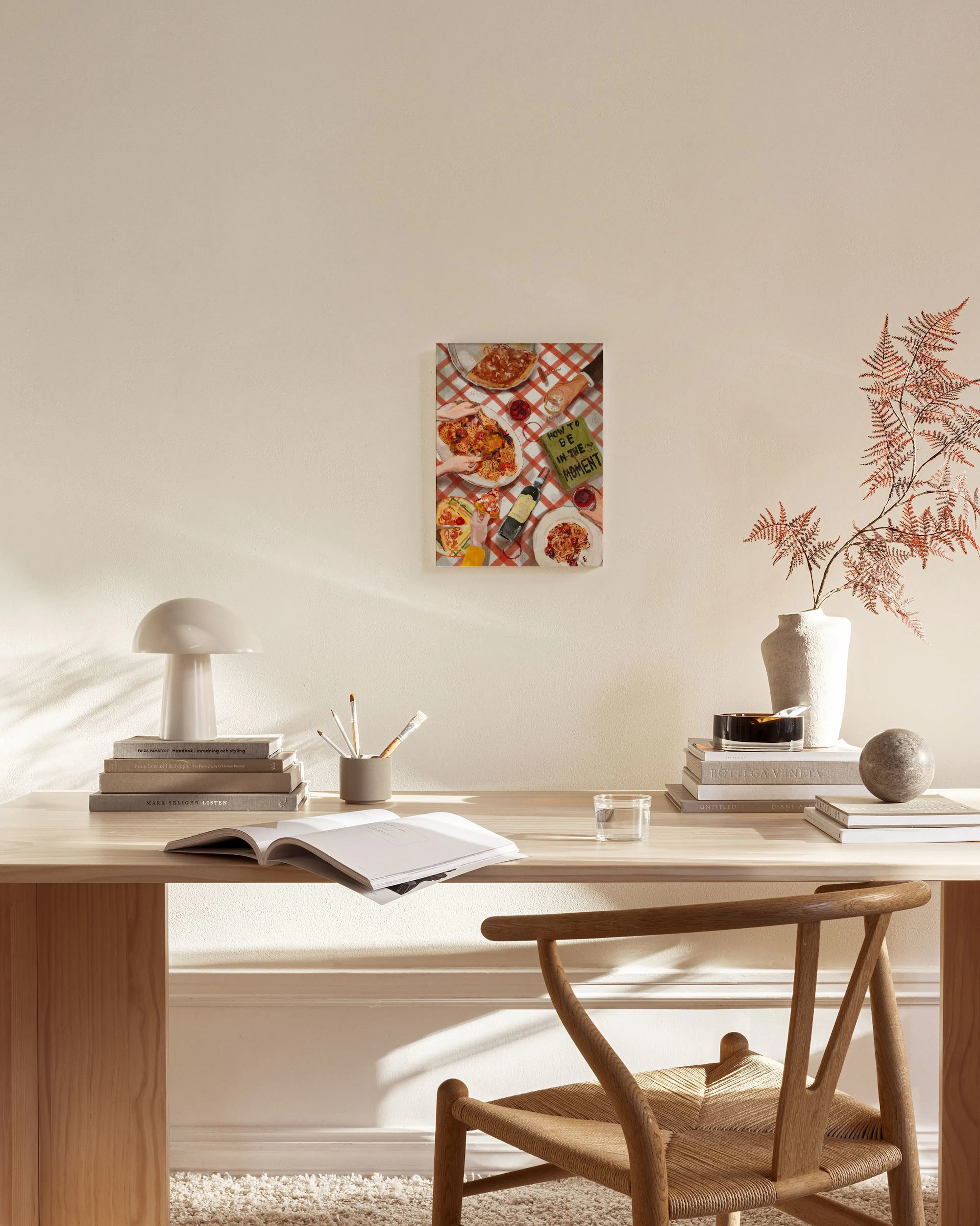 Tela decorativa de uma mesa de jantar com toalha xadrez vermelha e branca, massas e pizza, pendurada na parede de uma sala de es