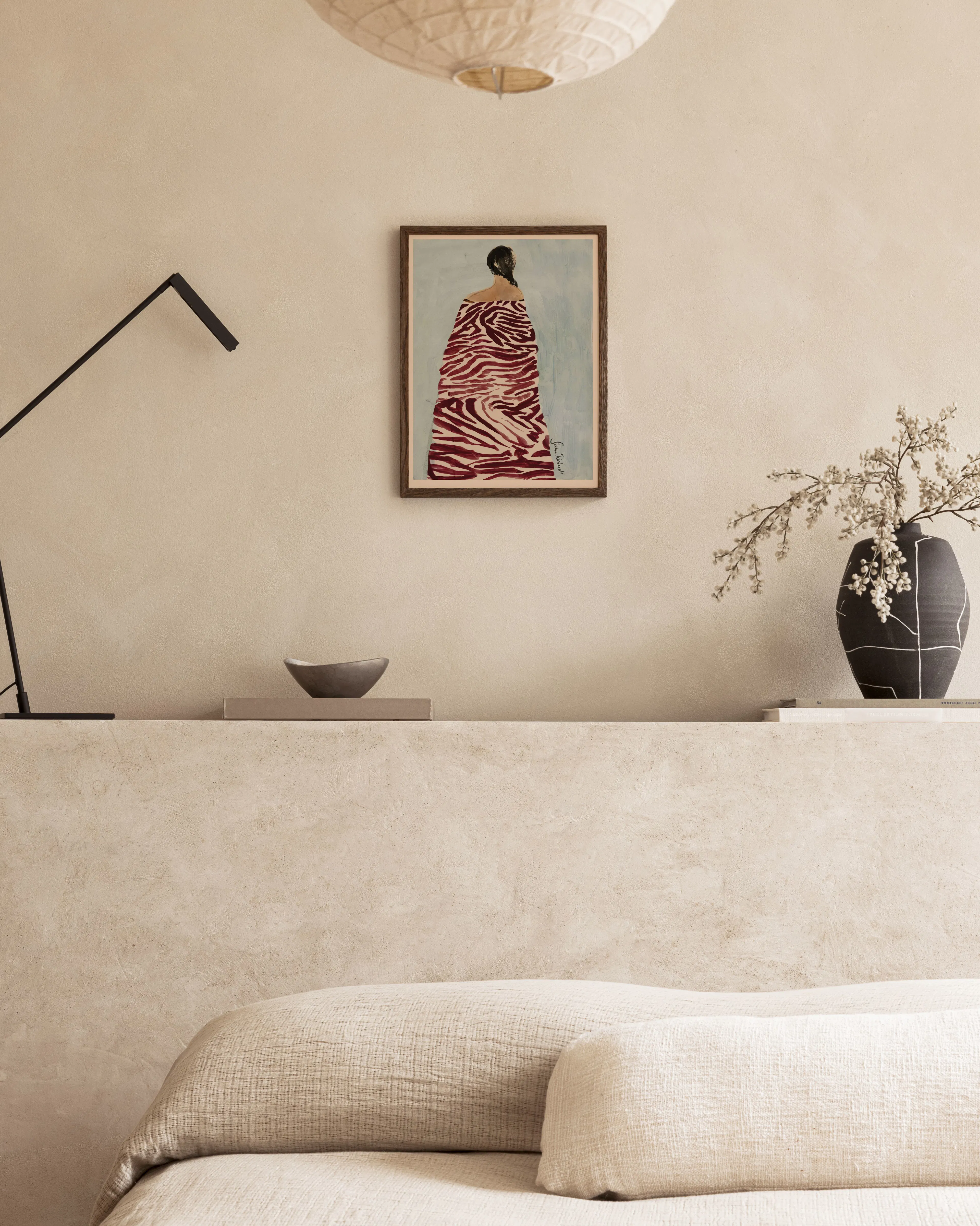 Poster av kvinna i rödvit zebrarandig klänning, hängandes ovanför en soffa i ett beige rum.