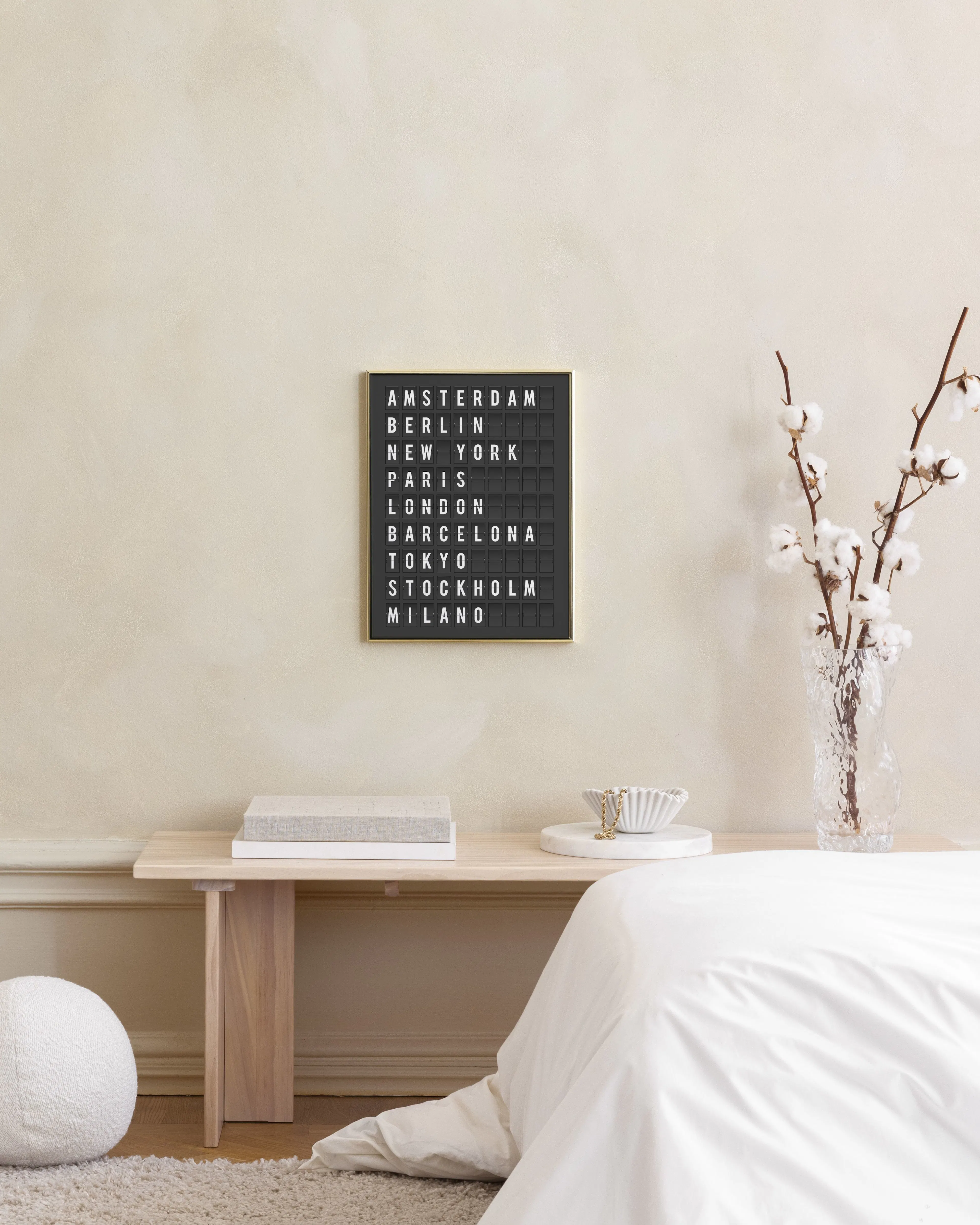 Affiche noire et blanche des noms de villes, suspendue au-dessus dune commode blanche avec des vases et une corbeille.