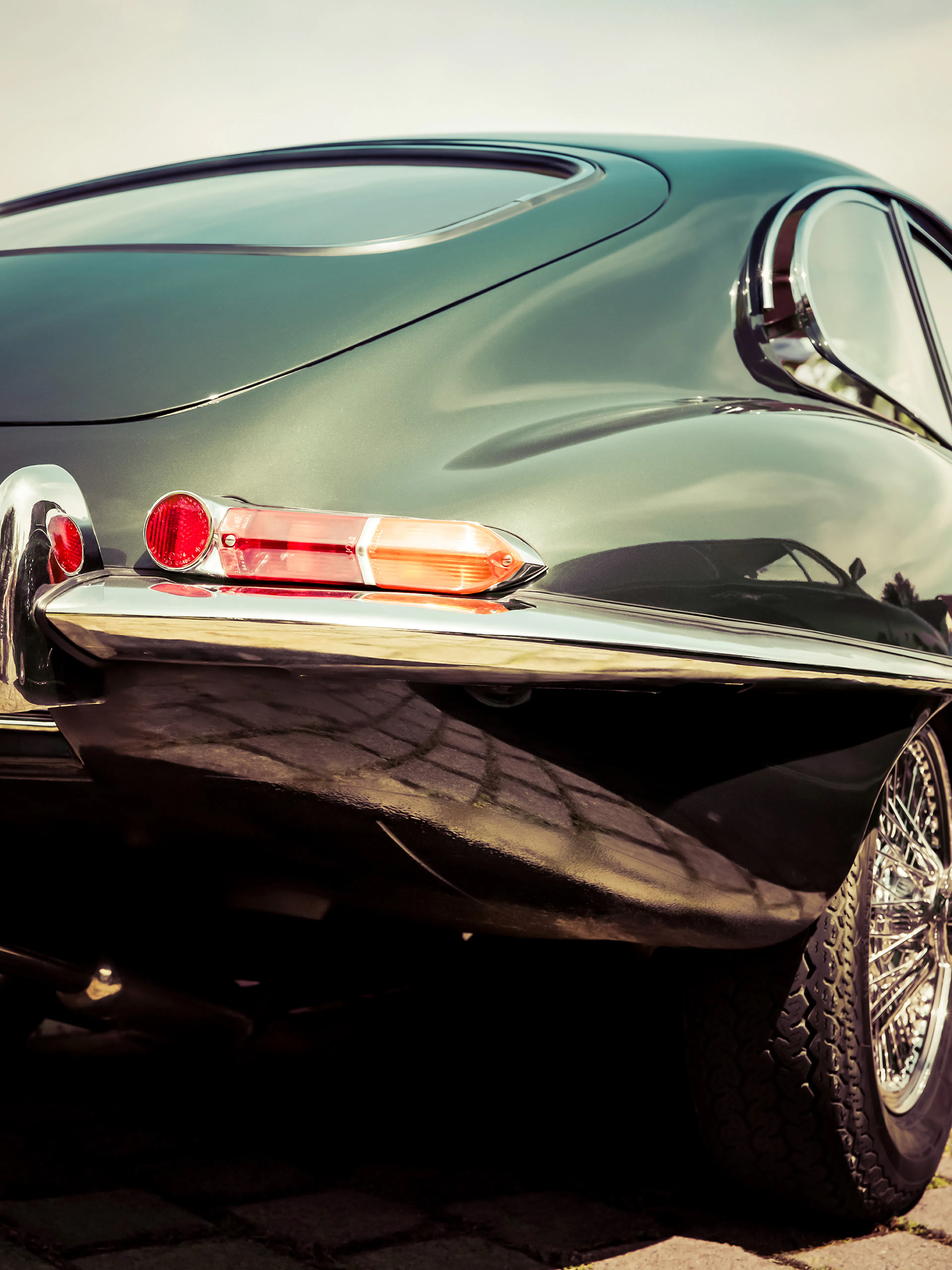 A print of a dark green vintage sports cars rear, featuring a red taillight and chrome details.