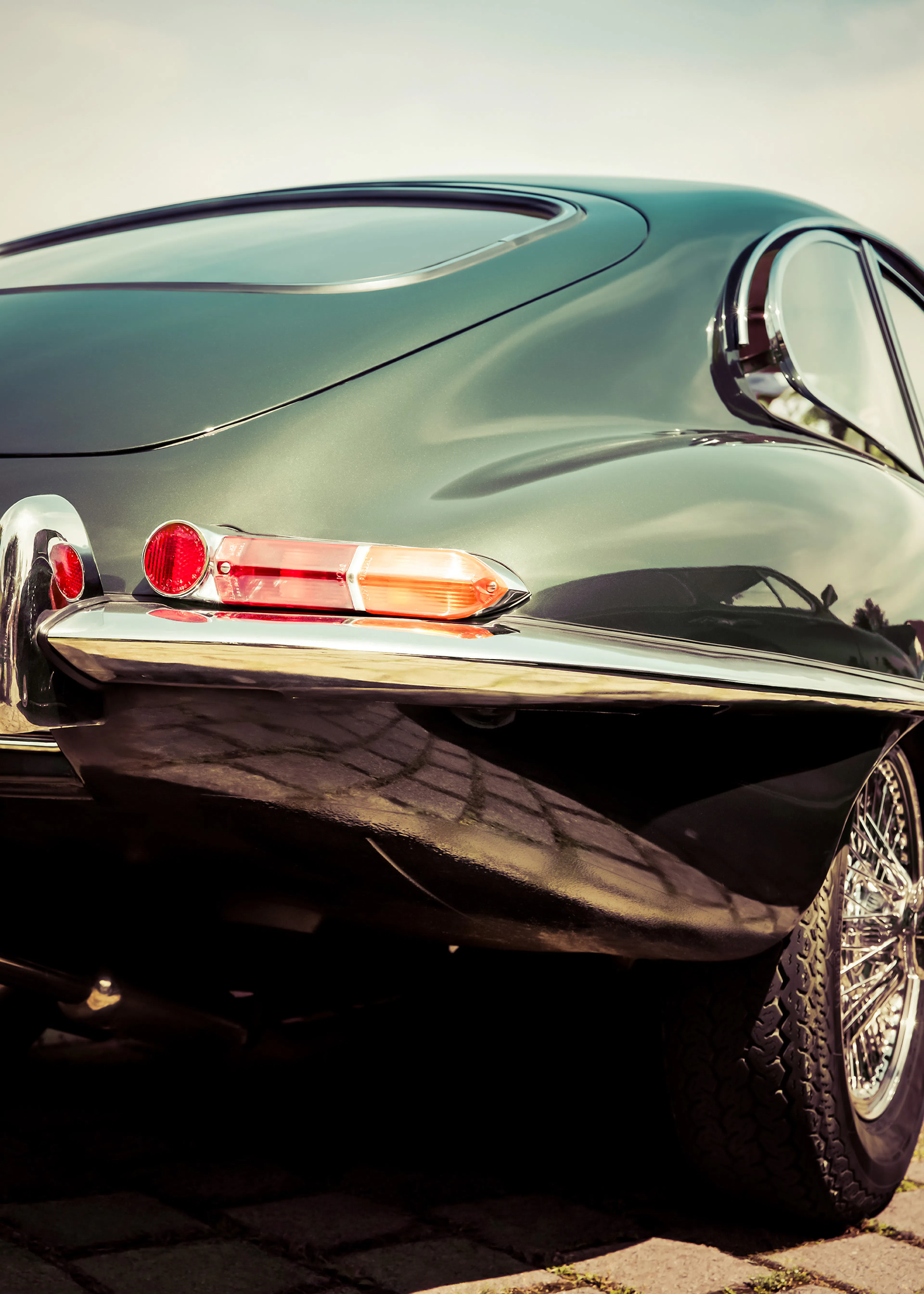 A print of a dark green vintage sports cars rear, featuring a red taillight and chrome details.