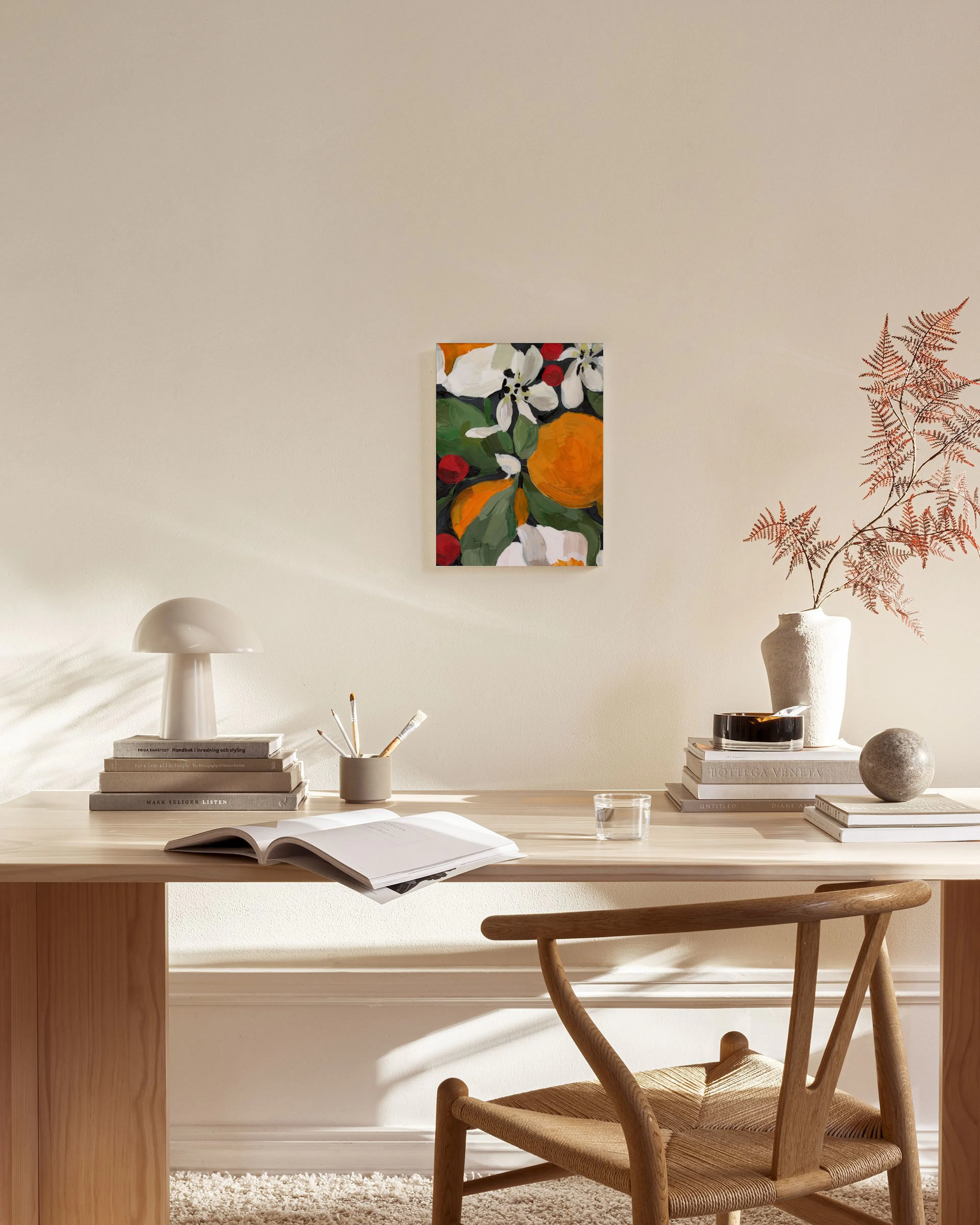 Lerretsbilde med oransje sitrusfrukter og hvite blomster, henger over et lavt trebord i en moderne stue.