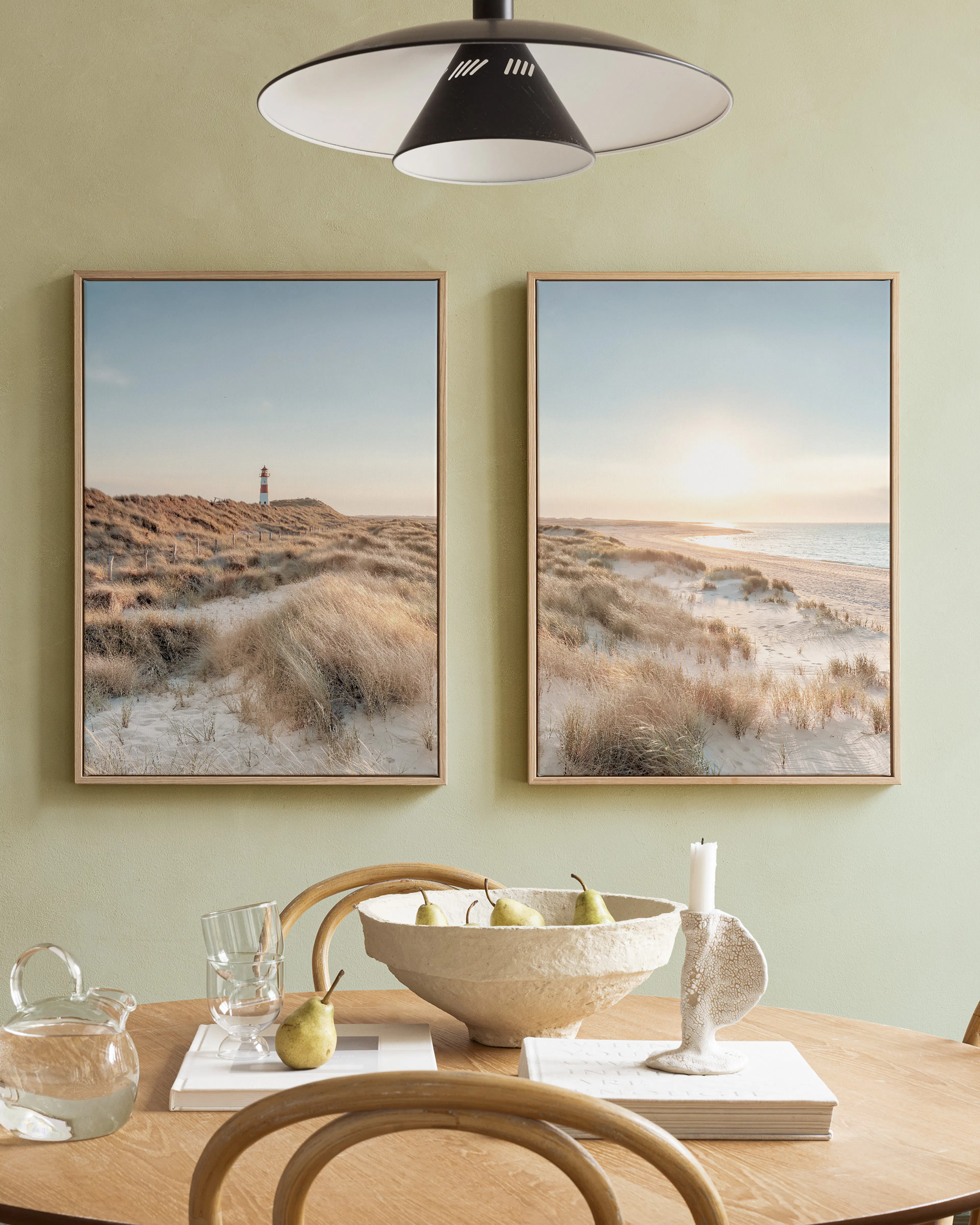 A poster pack of two beach landscape prints, one with sand dunes and sun, the other with a lighthouse, displayed above a wooden 
